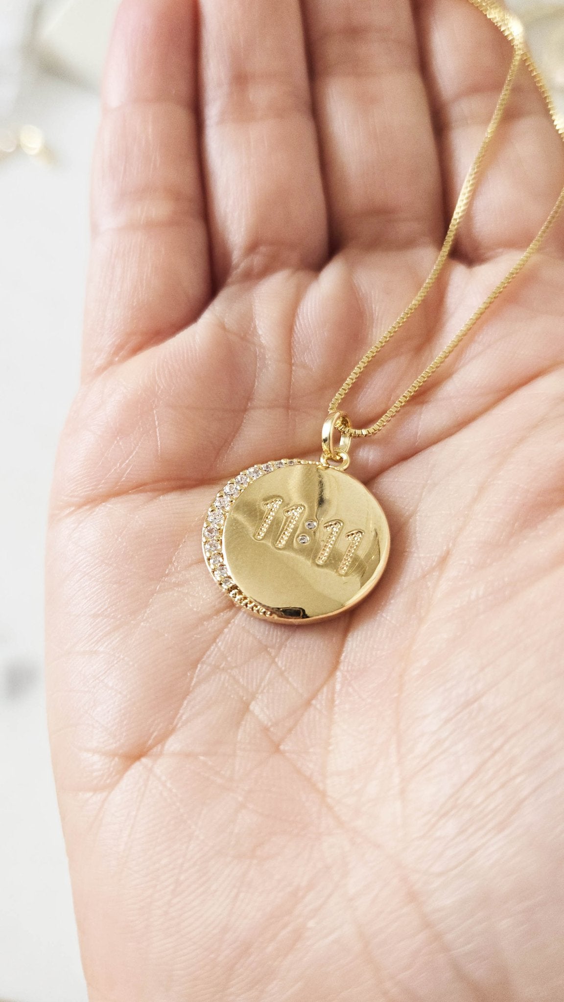 A 11:11 crystal pendant in palm on a gold-filled chain.