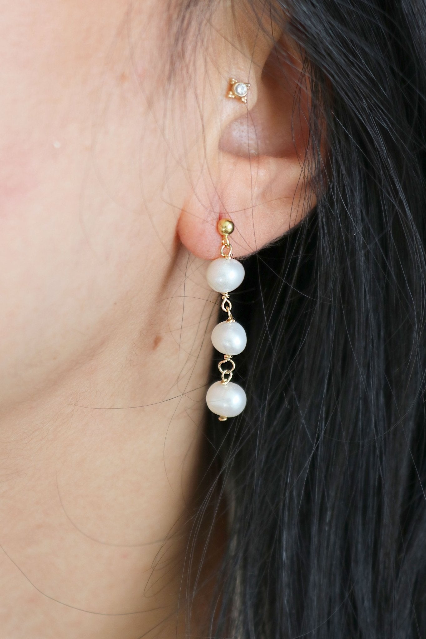 Tri-pearl drop earring studs dangle from a woman's ear. 