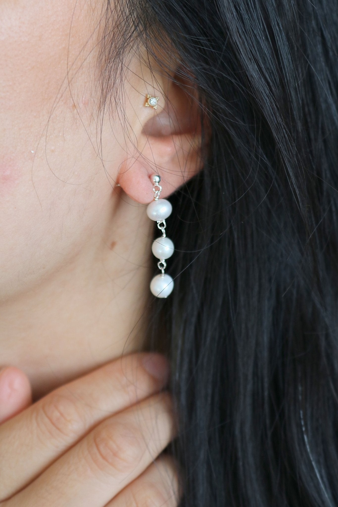 Tri-pearl drop earring studs dangle from a woman's ear. 