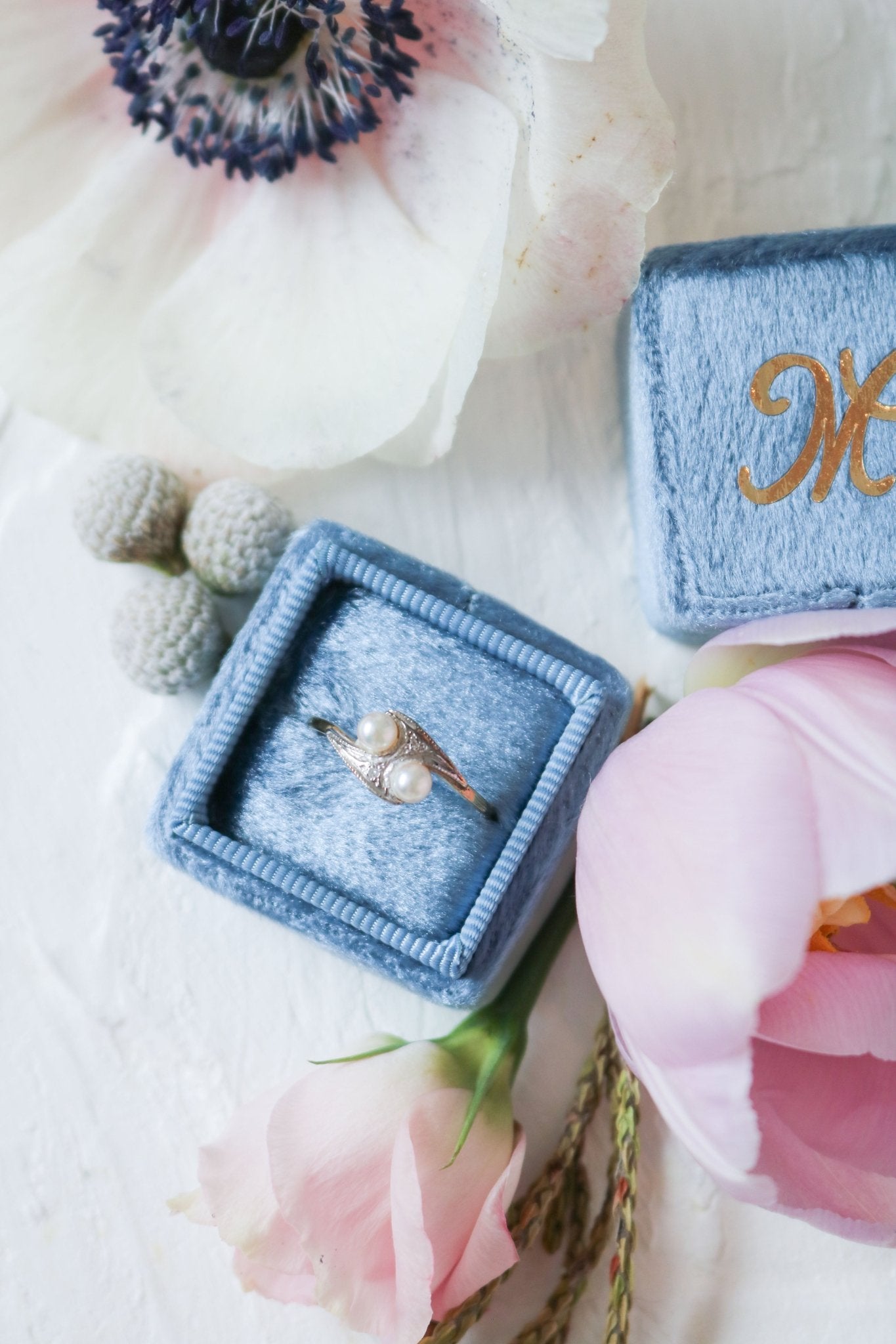 A Double Pearl and Diamond Vintage Engagement Ring 9ct Yellow White Gold 1920 Art Nouveau Style sits in a blue ring box with flowers. 