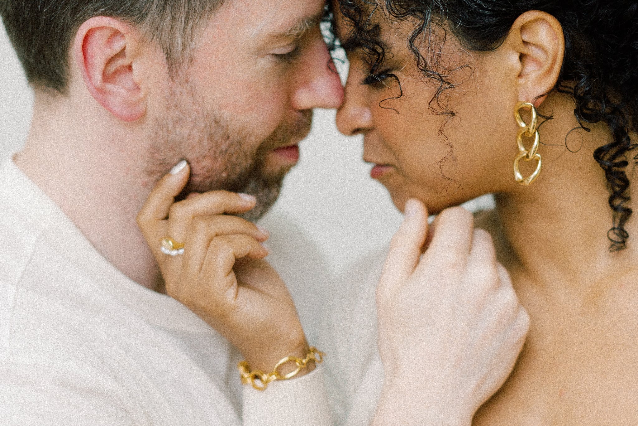 Close-up of a man and woman facing each other with woman wearing handmade gold jewelry on white background