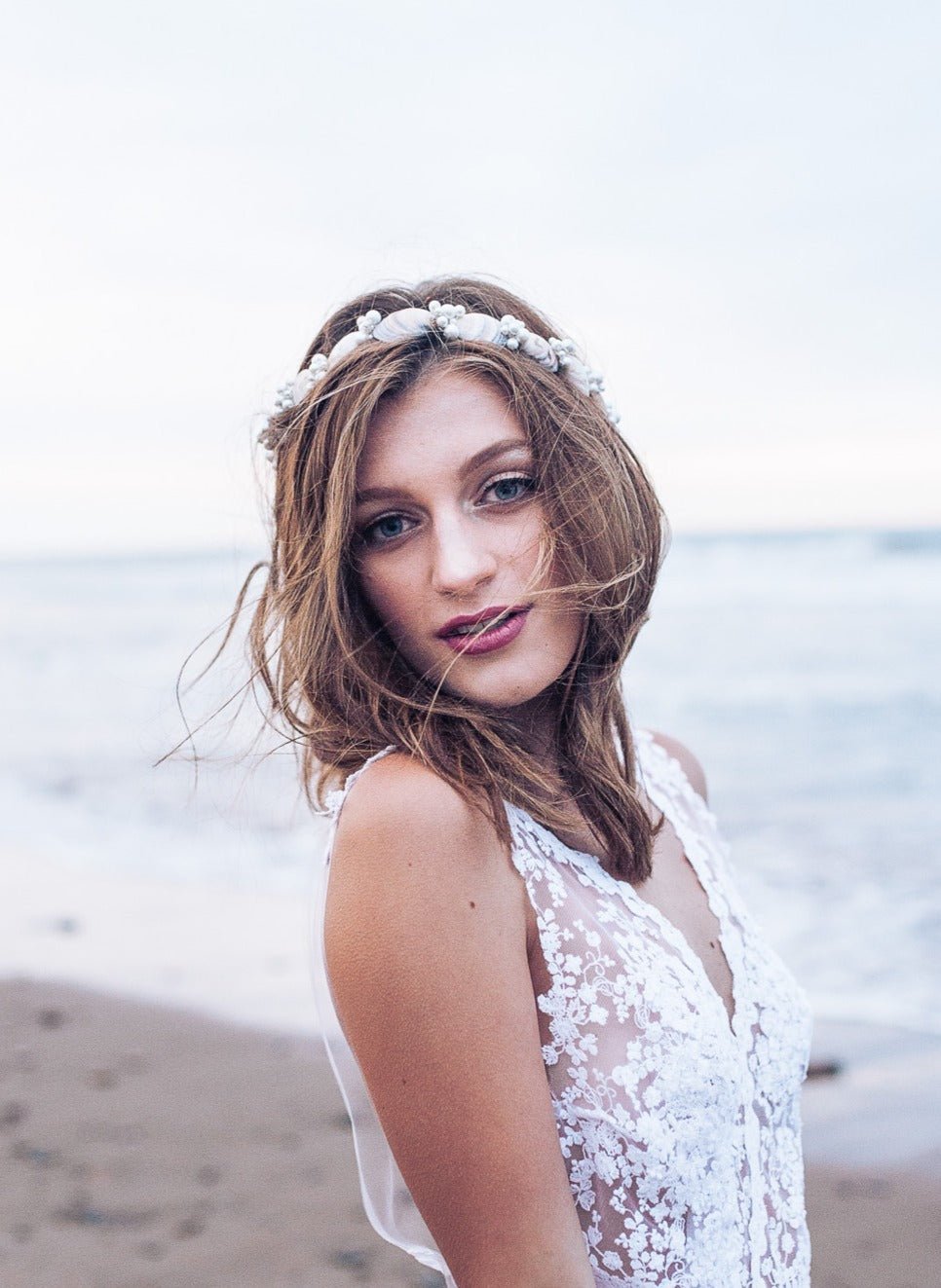 Windswept bride in sheer lacey wedding dress displays a fresh take on seas inspired hair wear with a seashell and pearl hairband. 