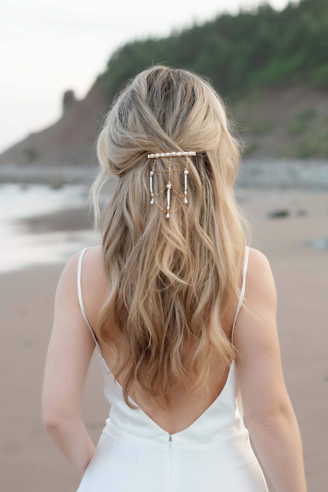 Golden netted hair chain and barrette with multiple freshwater pearls cascades down a wave of blonde hair on a bride by the ocean. 