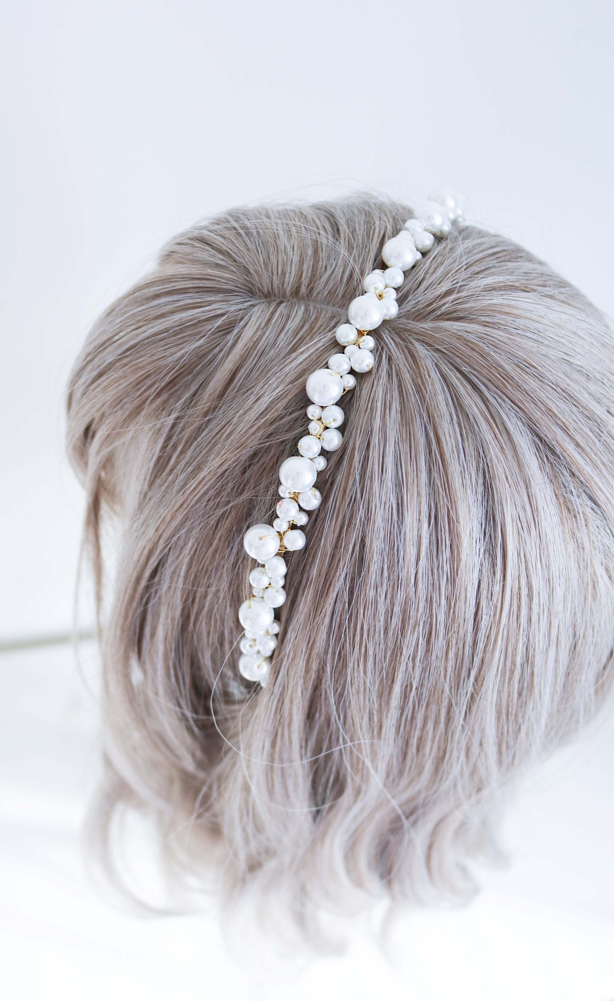 A wire-wrapped wedding pearl headband in gold displayed on a wigged head bust. 