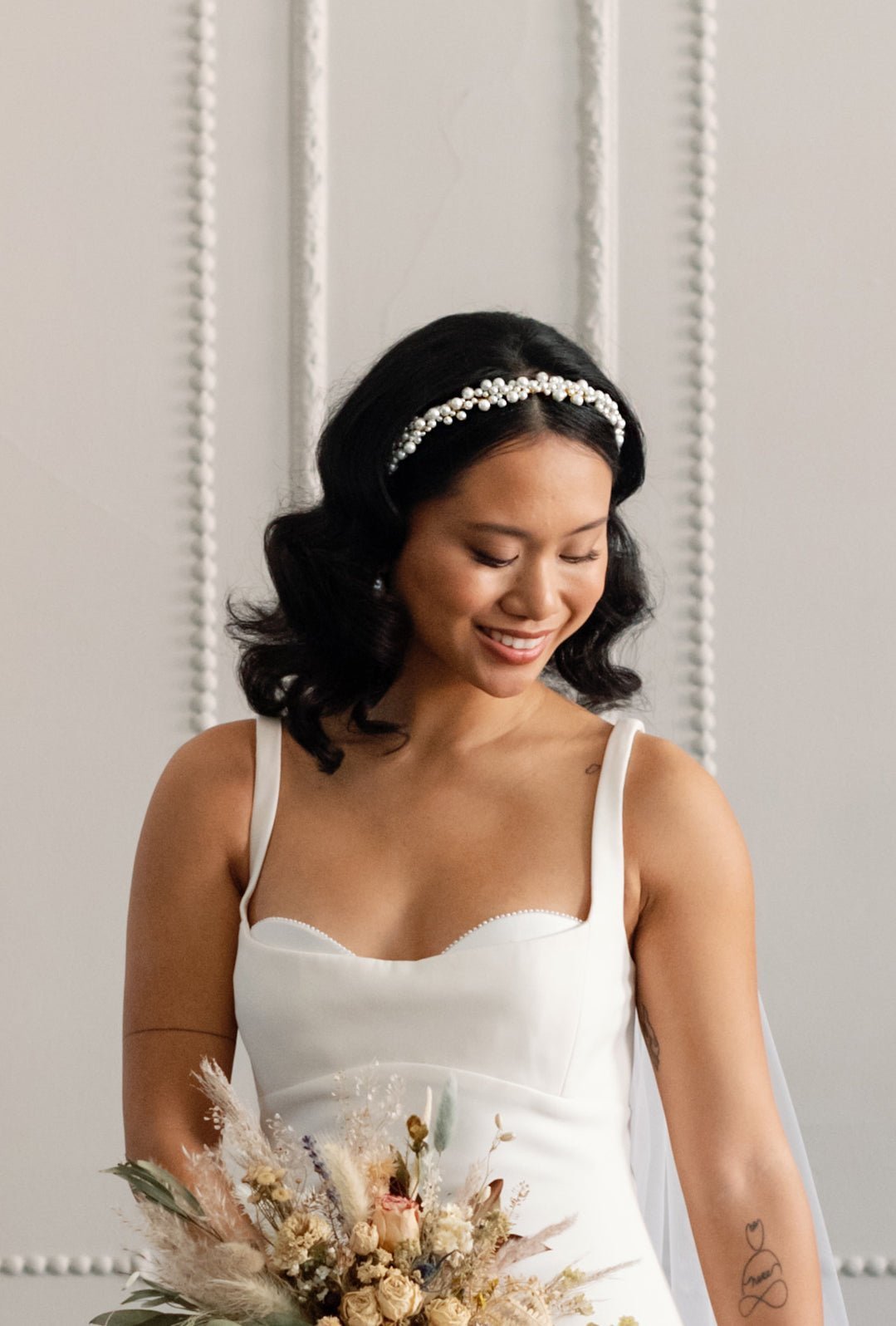 Happy bride holding bouquet wearing a large pearl-wrapped bridal headband on her wedding day. 