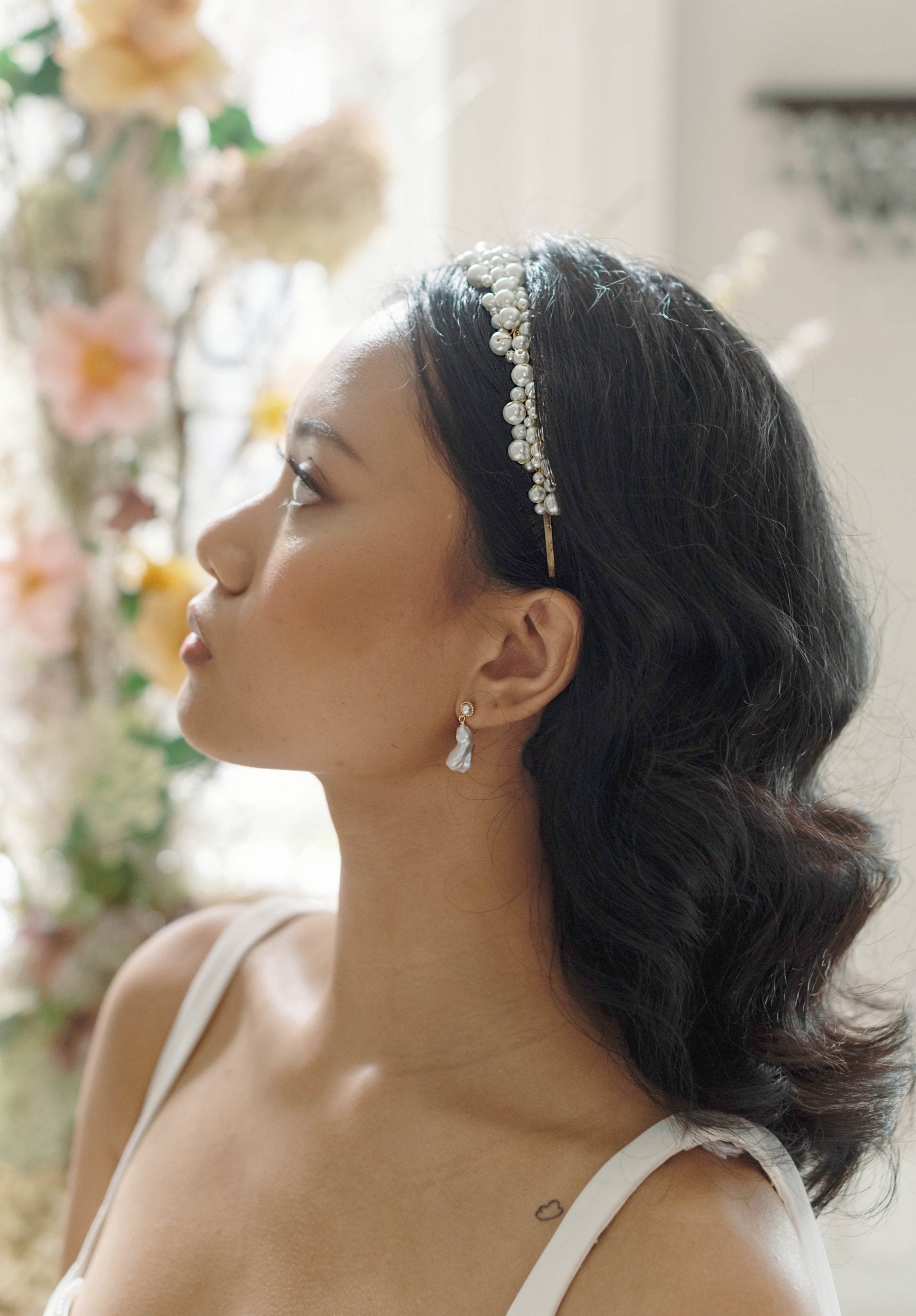 BIPOC bride side profile wearing a bridal pearl headband with wire-wrapped Swarovski pearls in Gold with blurred background.