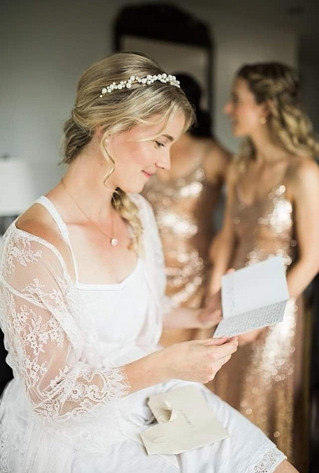 Bride in white wedding dress sitting, reading card wearing clustered Swarovski pearl bridal headband with bridesmaids in background. Handmade Canadian Accessories & Pearl Bridal Hair Accessories by Small Canadian jewelry brand.