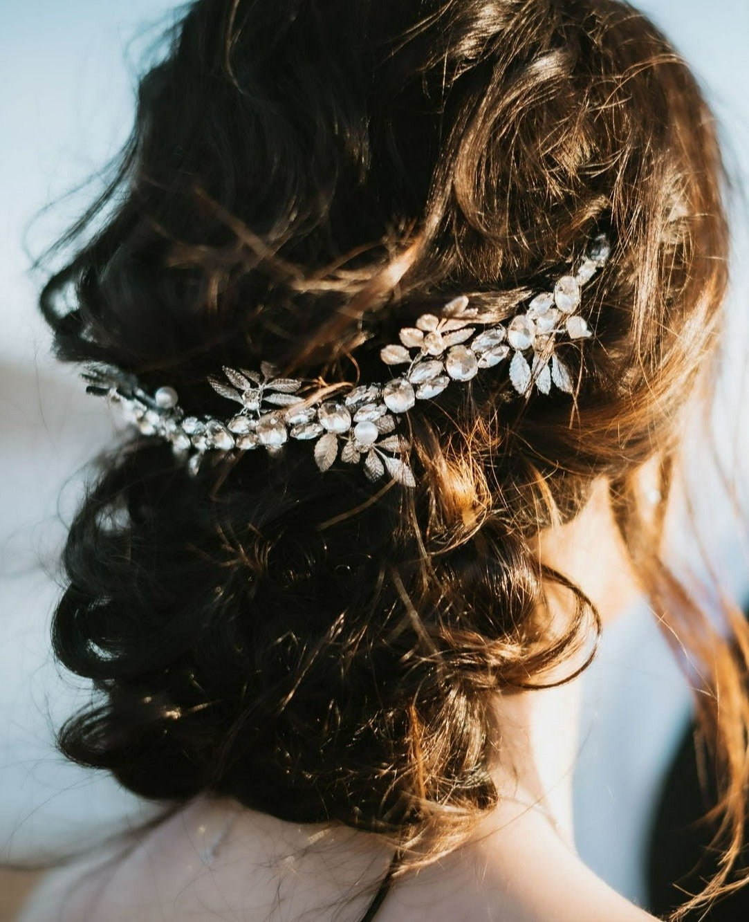 Silver Anwen Crystal & Leaf Crown Bridal Hair Accessory Sitting on Top of Curly Dark Hair Bun. 