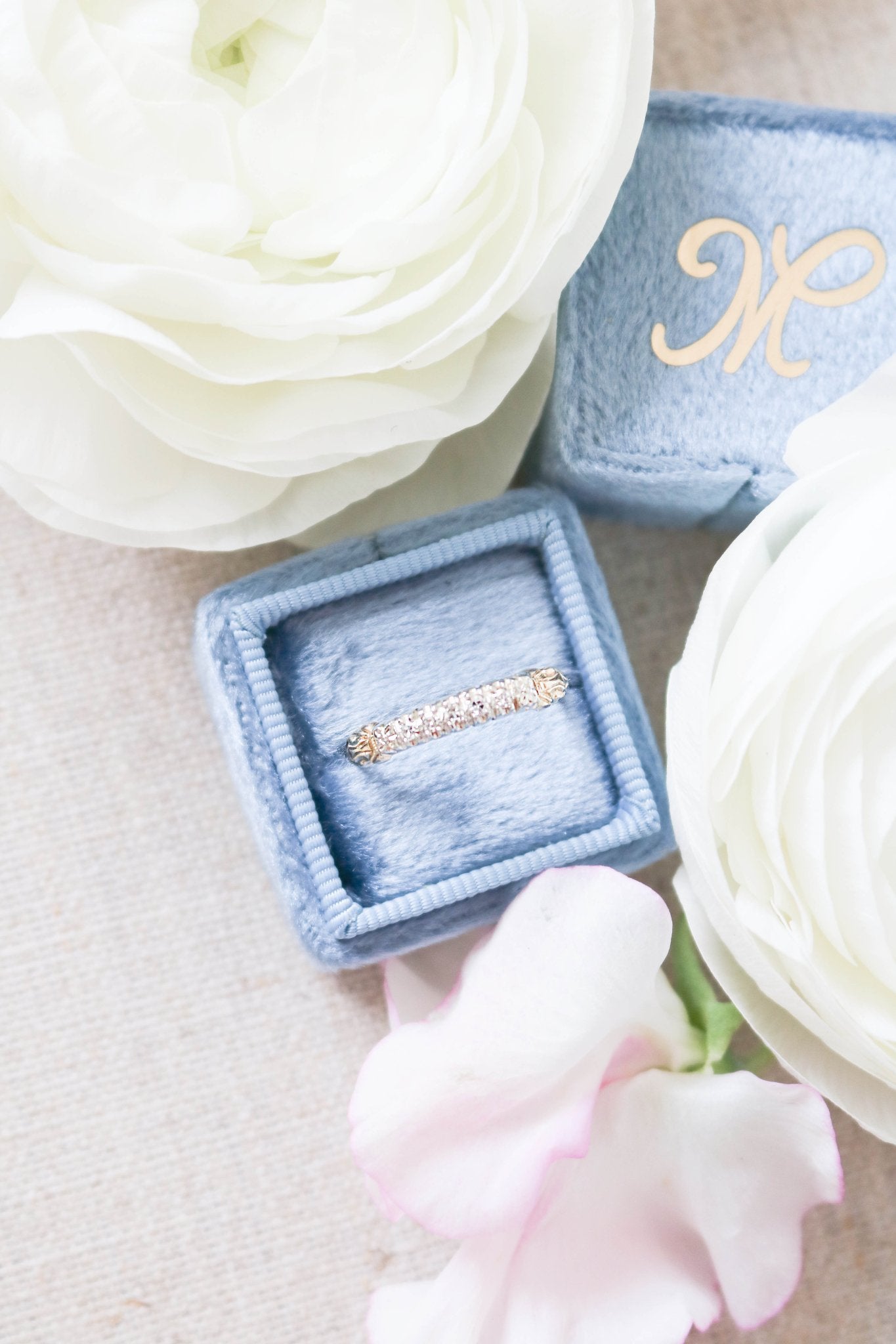 Art Deco vintage engagement ring with multiple diamonds sits in a box next to large flowers. 