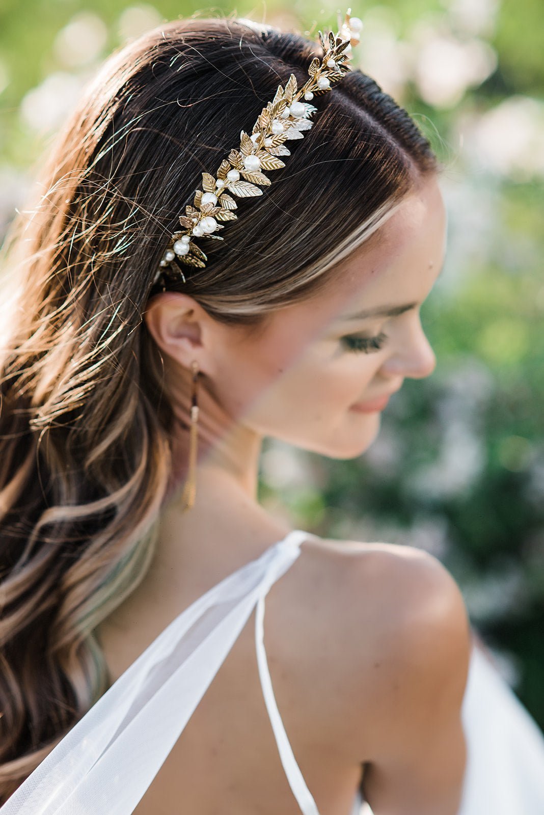 A bride looks aside bashfully while wearing a fancy bridal crown with tiers of leaves and stacked with pearls. 