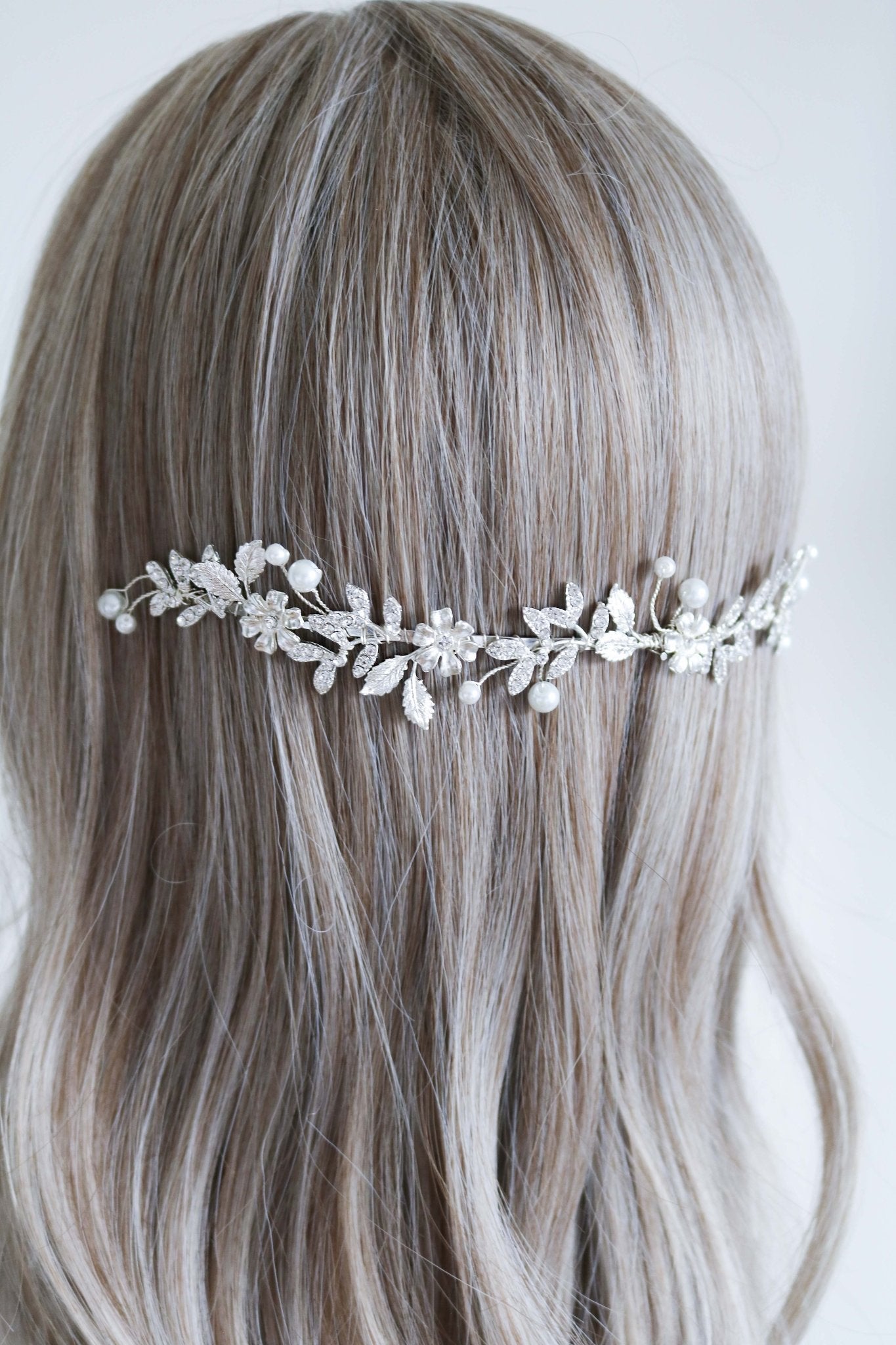 Silver wedding headband with crystal leaves, flowers, and freshwater pearls sits behind a head of hair. 