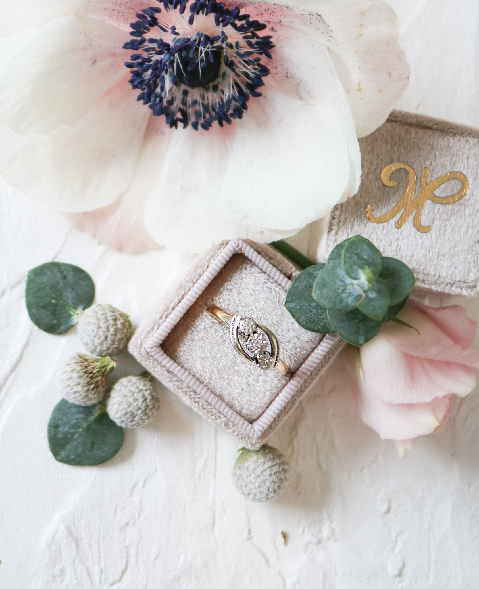 A vintage engagement ring in 18ct gold and platinum with diamonds sits in a ring box surrounded by flora. 