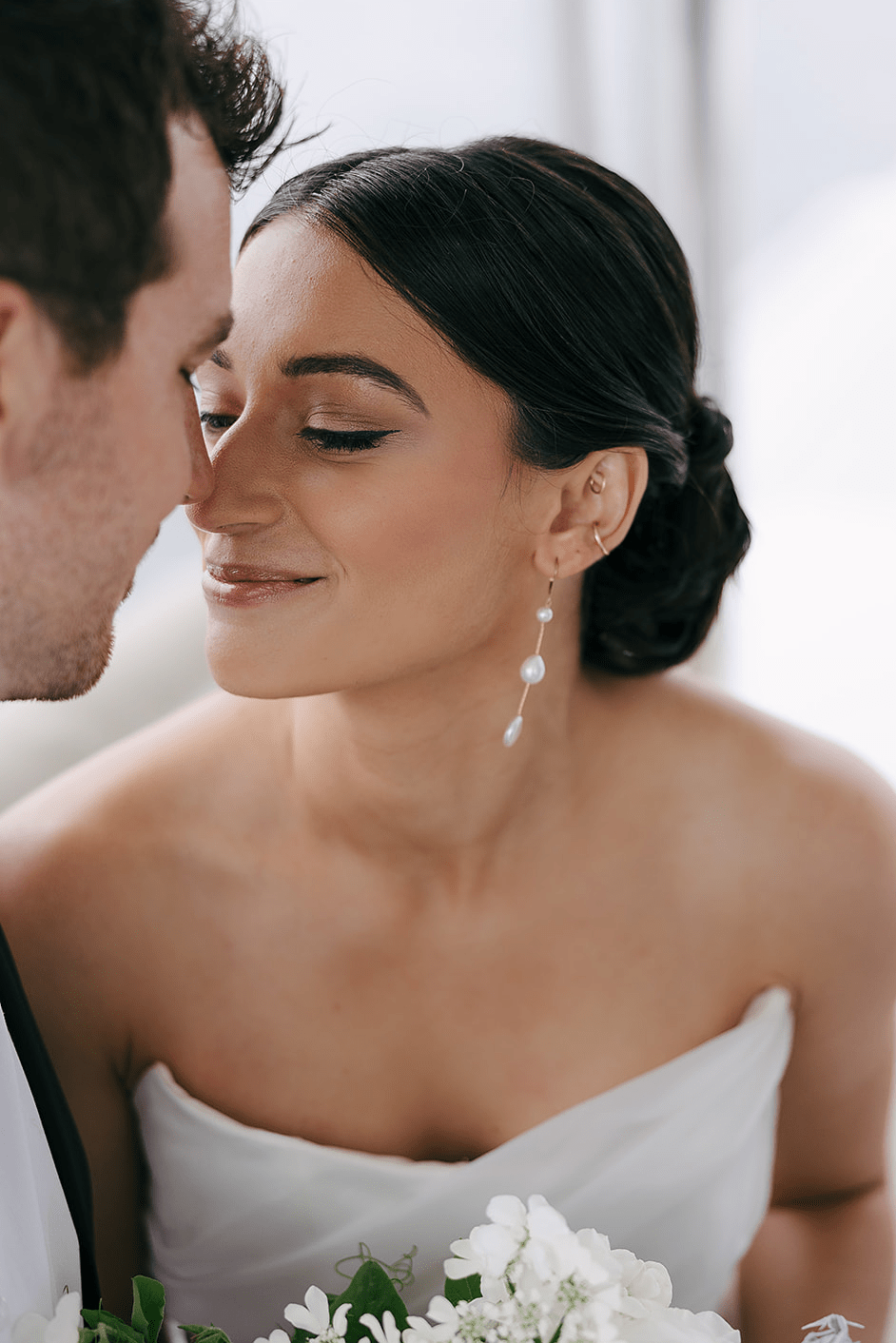 Bride and groom touch noses while bride showcases her Aura gold filled freshwater pearl dangle bridal earrings.