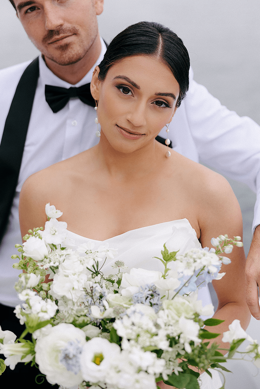 Bride with bridal flower bouquet and Aura gold filled fresh water pearl dangle earrings stands in front of her groom. Pearl Bridal jewelry Canada.