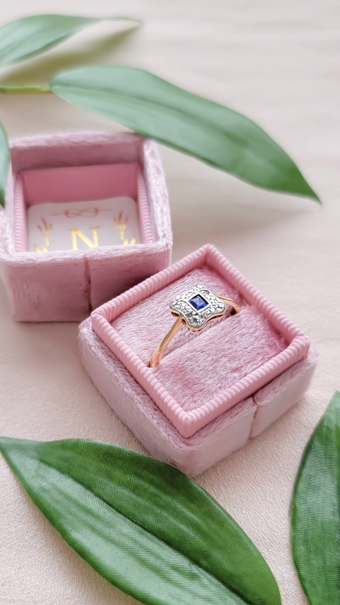 Aurora 18k Yellow Gold and Platinum Diamond Sapphire Engagement Ring  in Art Deco style in a pink ring box surrounded by leaves. Canadian vintage engagement rings. Bridal jewelry Canada. Vintage engagement rings Canada. Canadian weddings. Wedding Canada. Woman-owned Canadian jewelry brand. Canadian jewelry business. Small Canadian jewelry brands. 