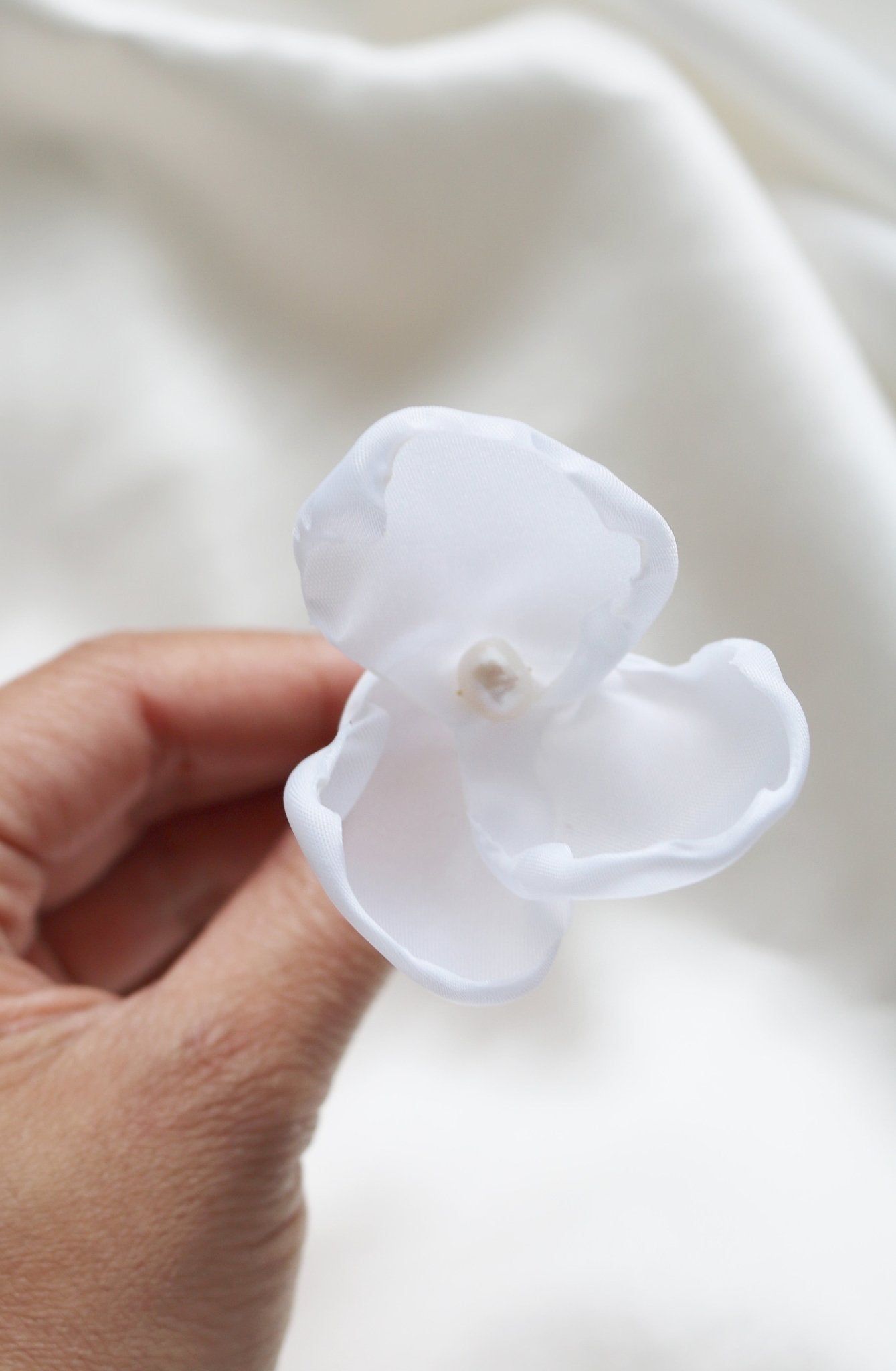 A single medium floral hairpin with a freshwater pearl is held up against a white background. 