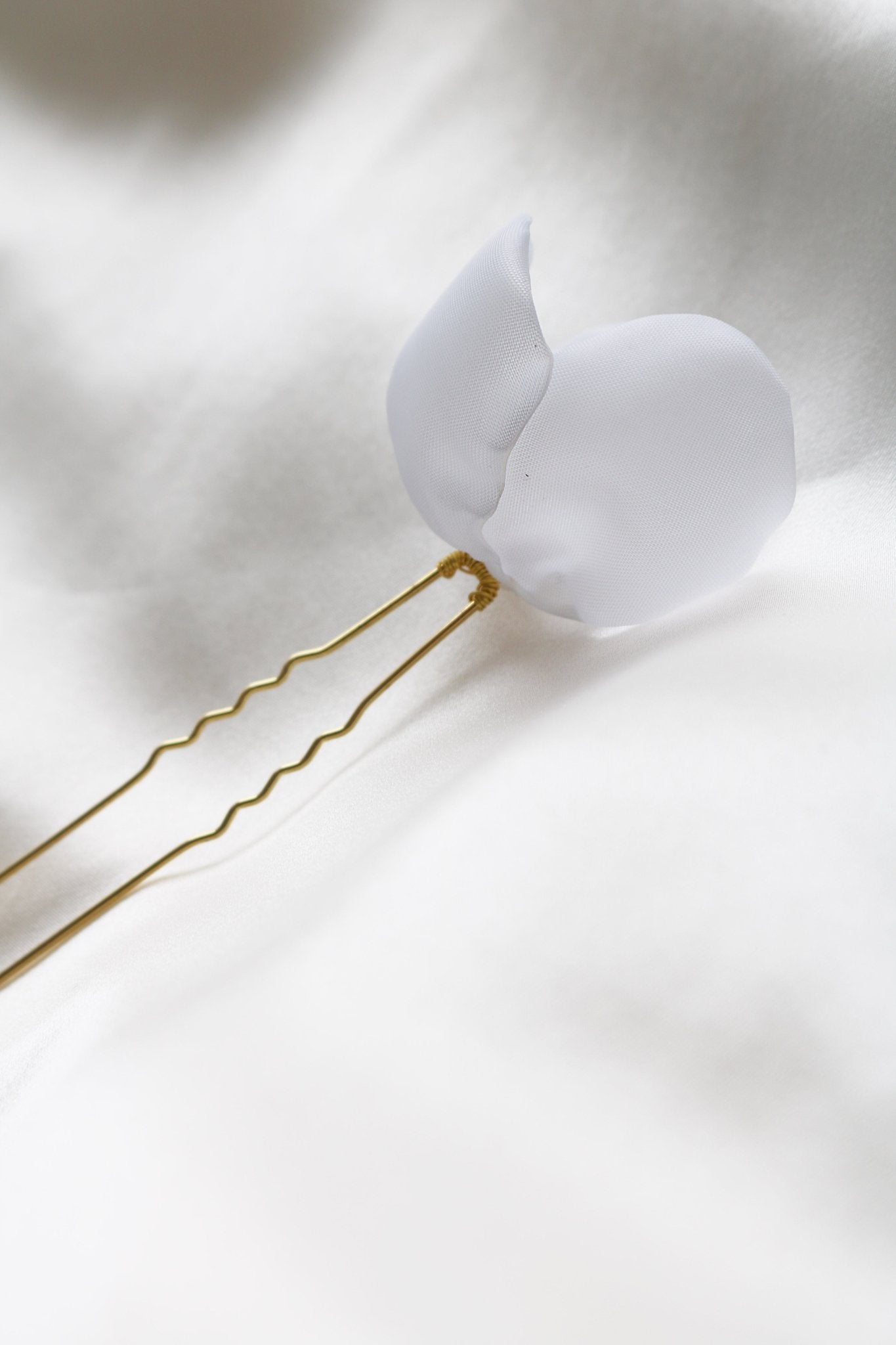 The back view of a gold bridal hairpin with fabric petals on white background. 