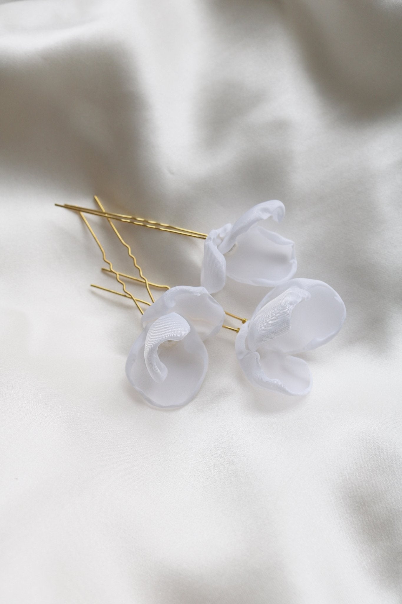 Three medium gold bridal hairpins with freshwater pearls on a satin sheet. 