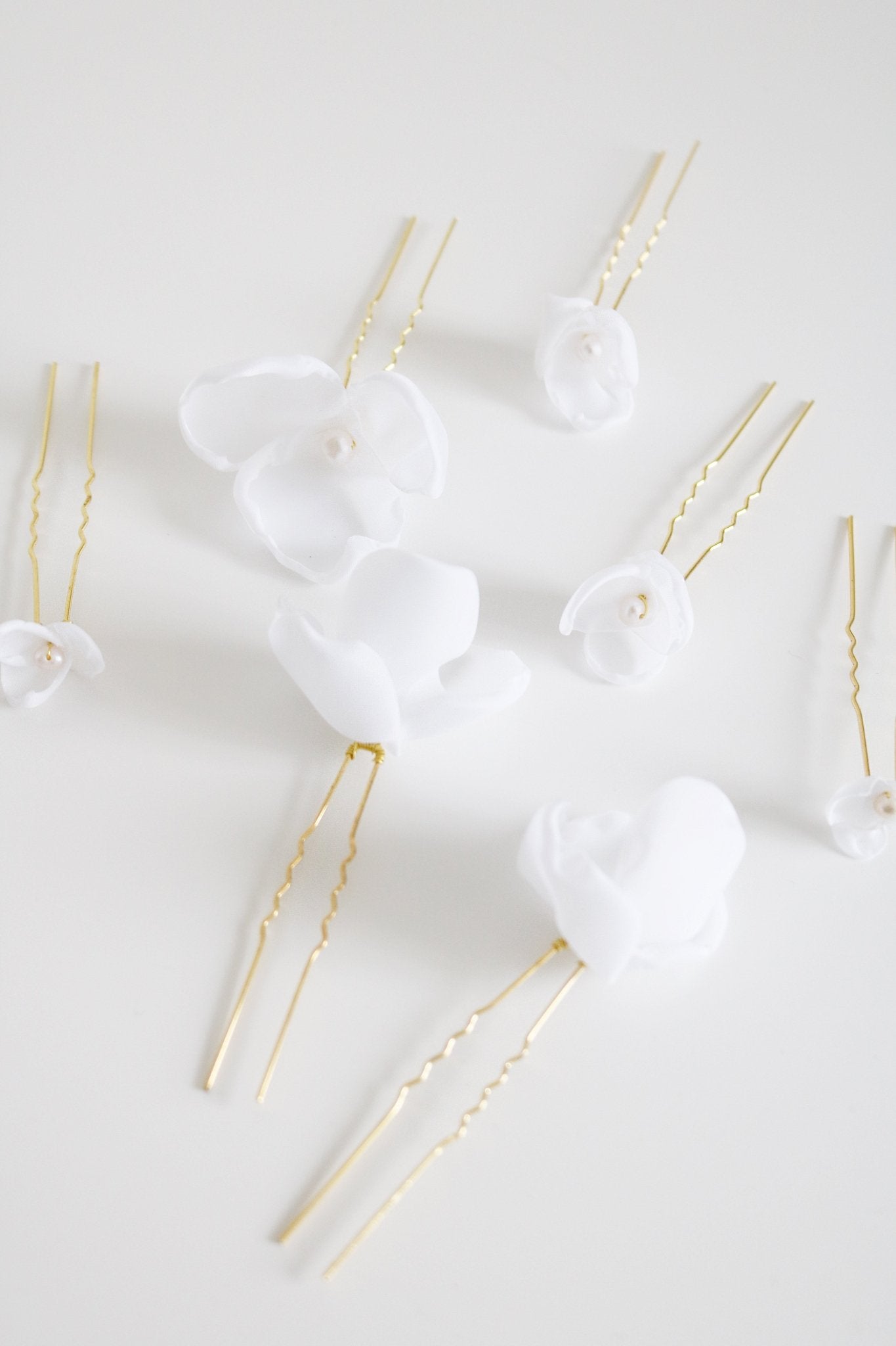 Multiple gold wedding hair accessories with fabric flowers and a freshwater pearl against white background. 