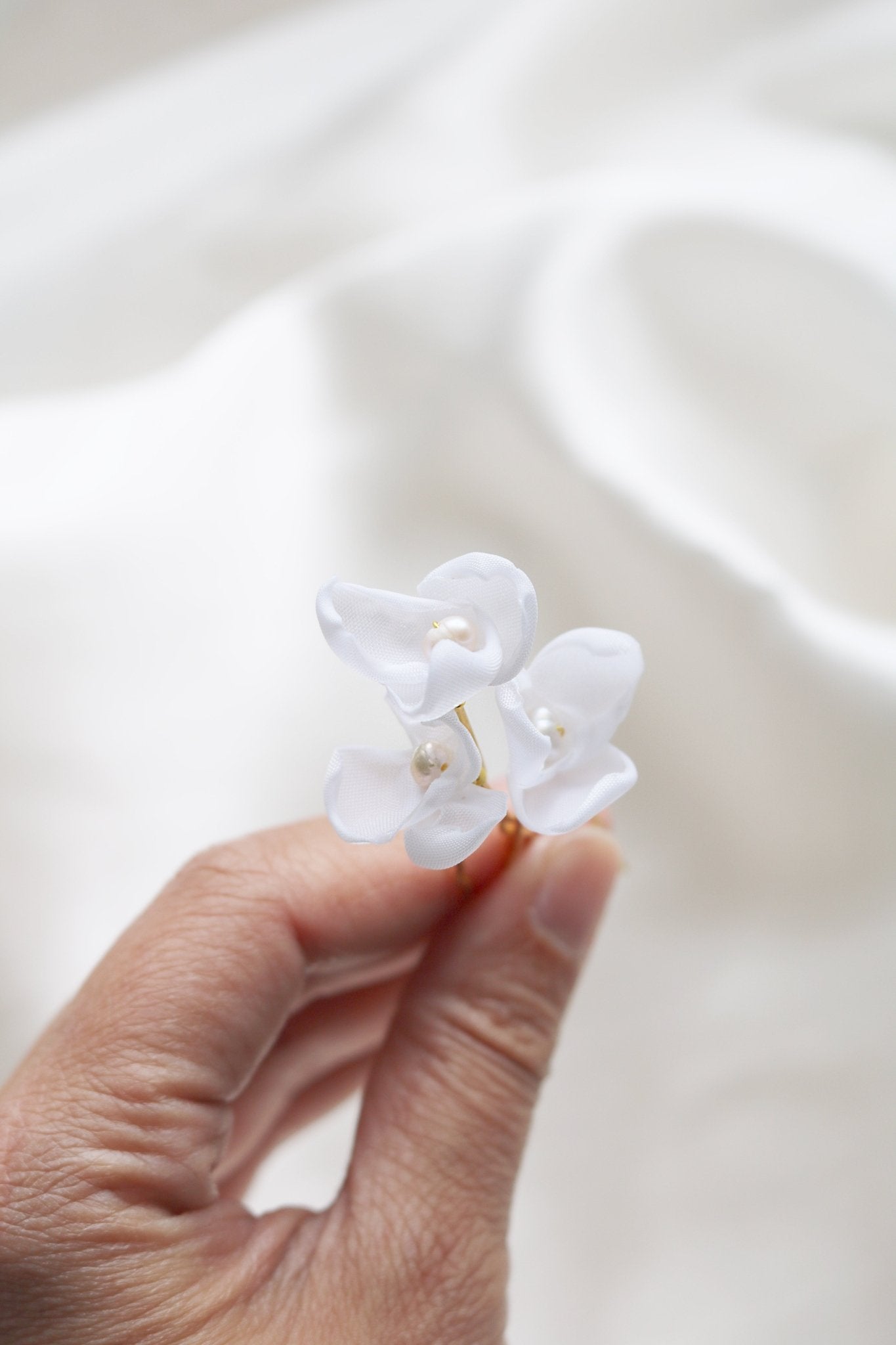 Several golden bridal hairpins with fabric flowers and freshwater pearls are held together like a tiny bouquet. 