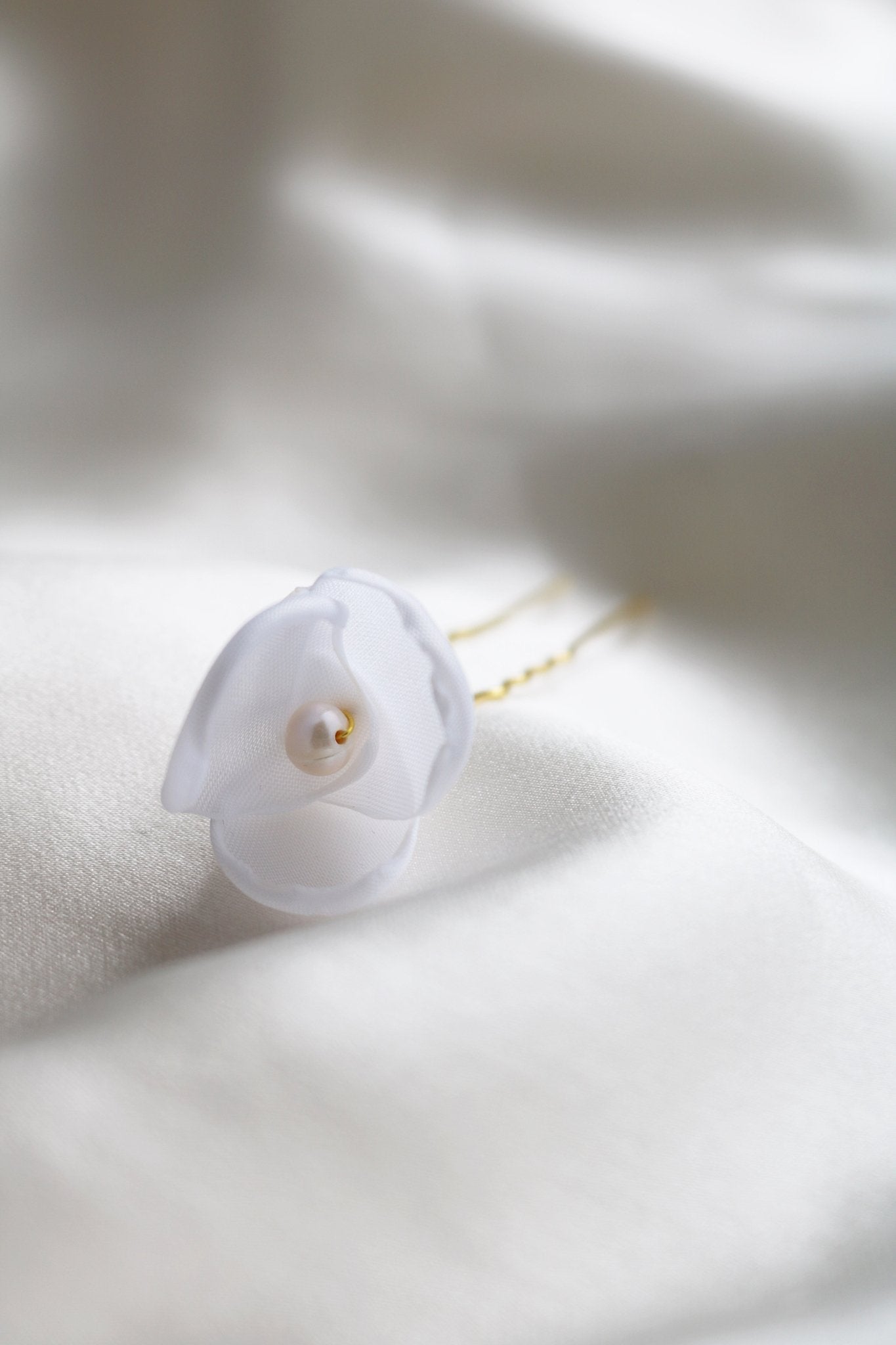 A Single Small Averie Floral Hairpin with fabric petals and freshwater pearl lays on a white satin sheet. 