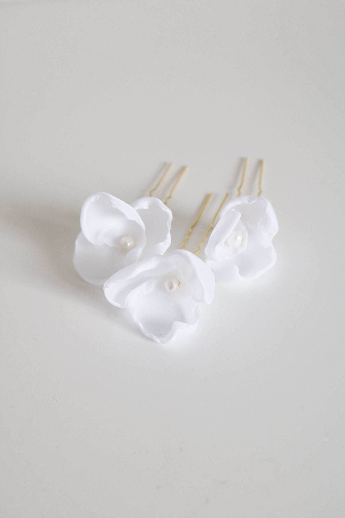 Close up of gold floral small bridal hairpins with organic pearls on white backdrop. 