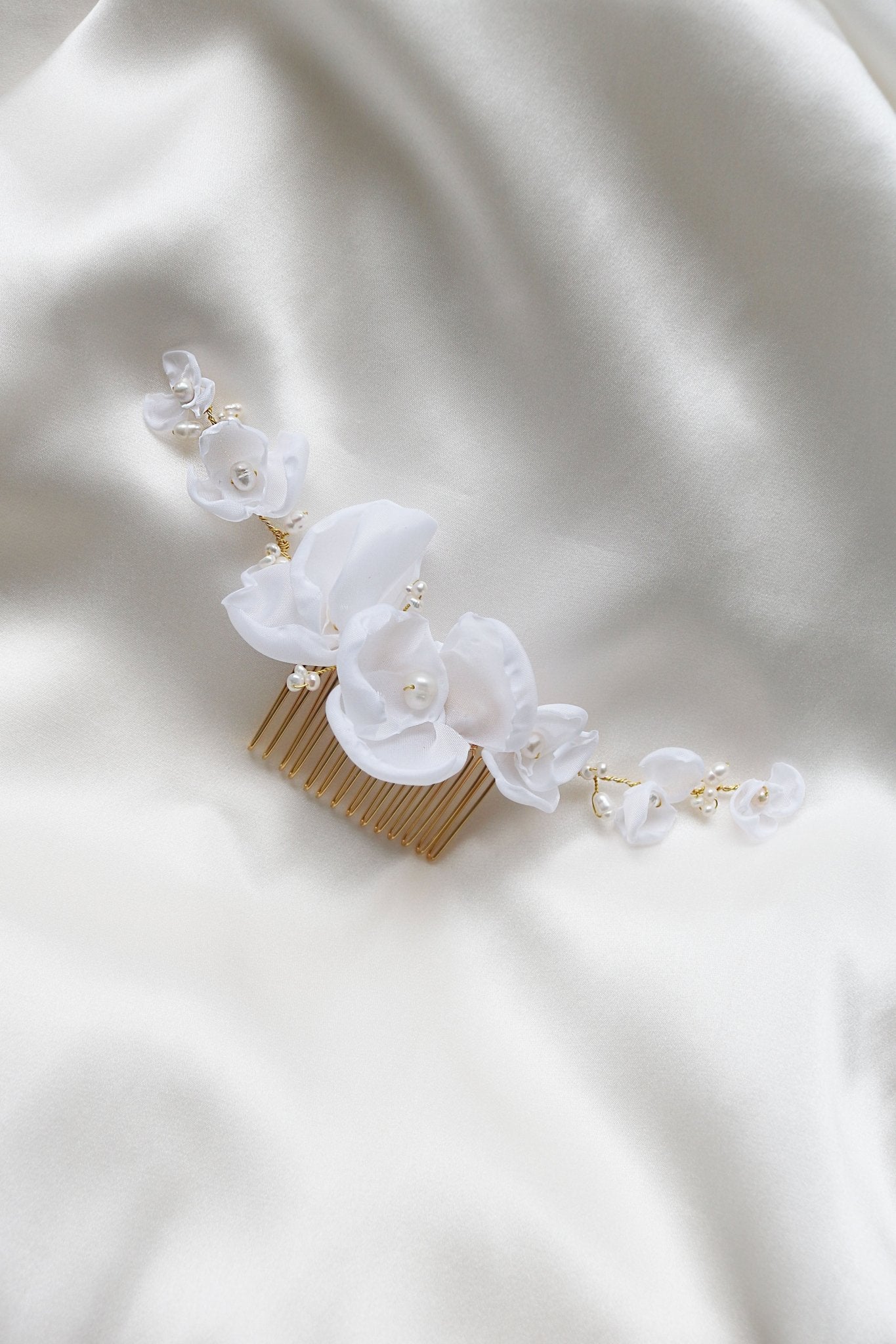 Averie Floral and Organic Freshwater Pearl Hairpiece laying on a white satin sheet. 