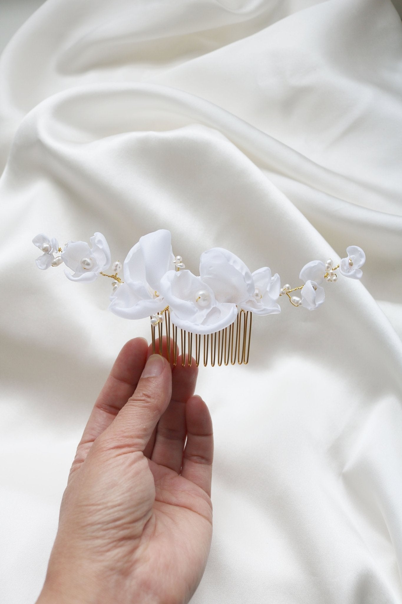 Averie Floral and Organic Freshwater Pearl Hairpiece for brides for weddings being held against a white satin sheet. 