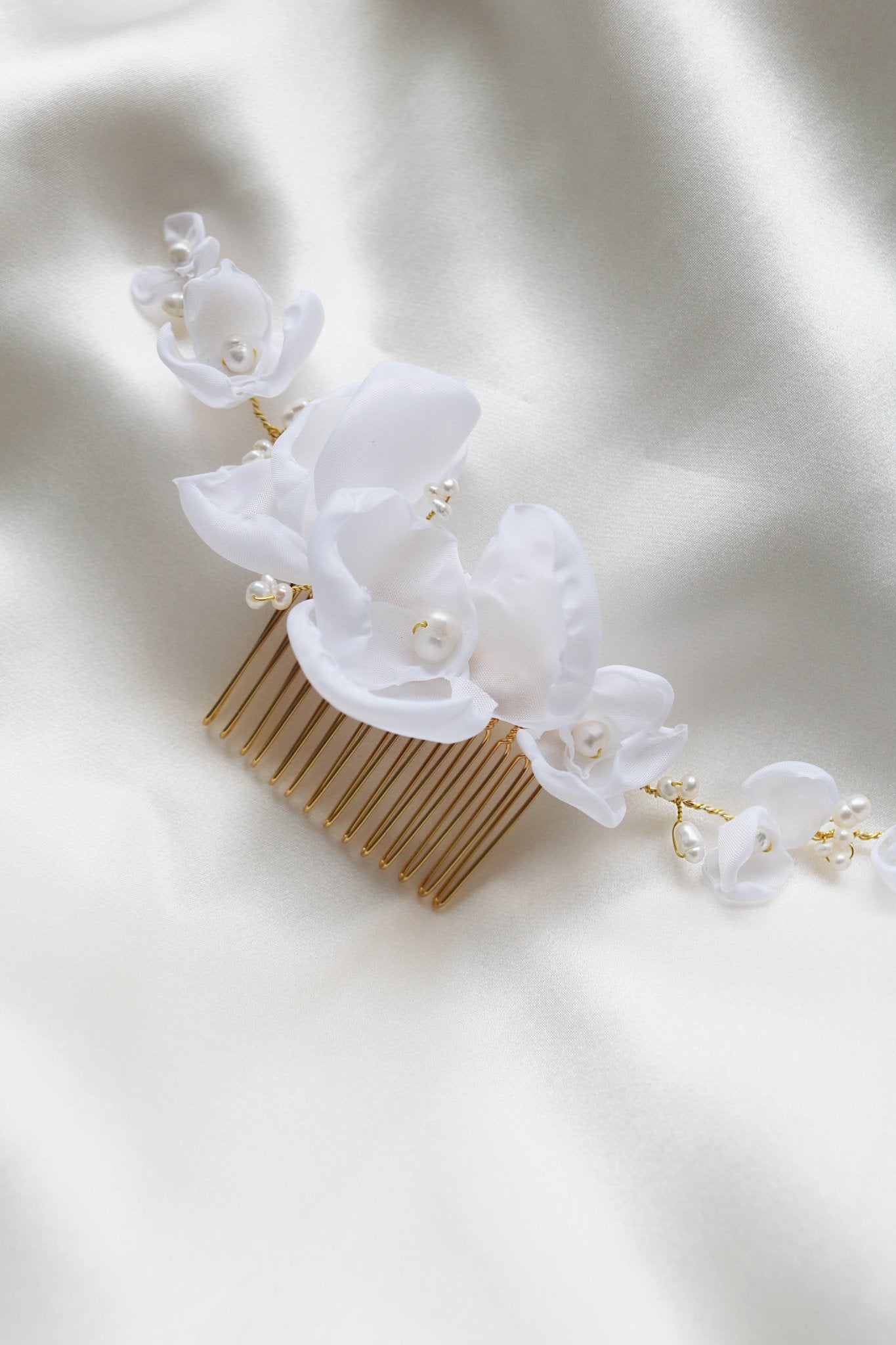 Averie Floral and Organic Freshwater Pearl Hairpiece laying on a white satin sheet. 