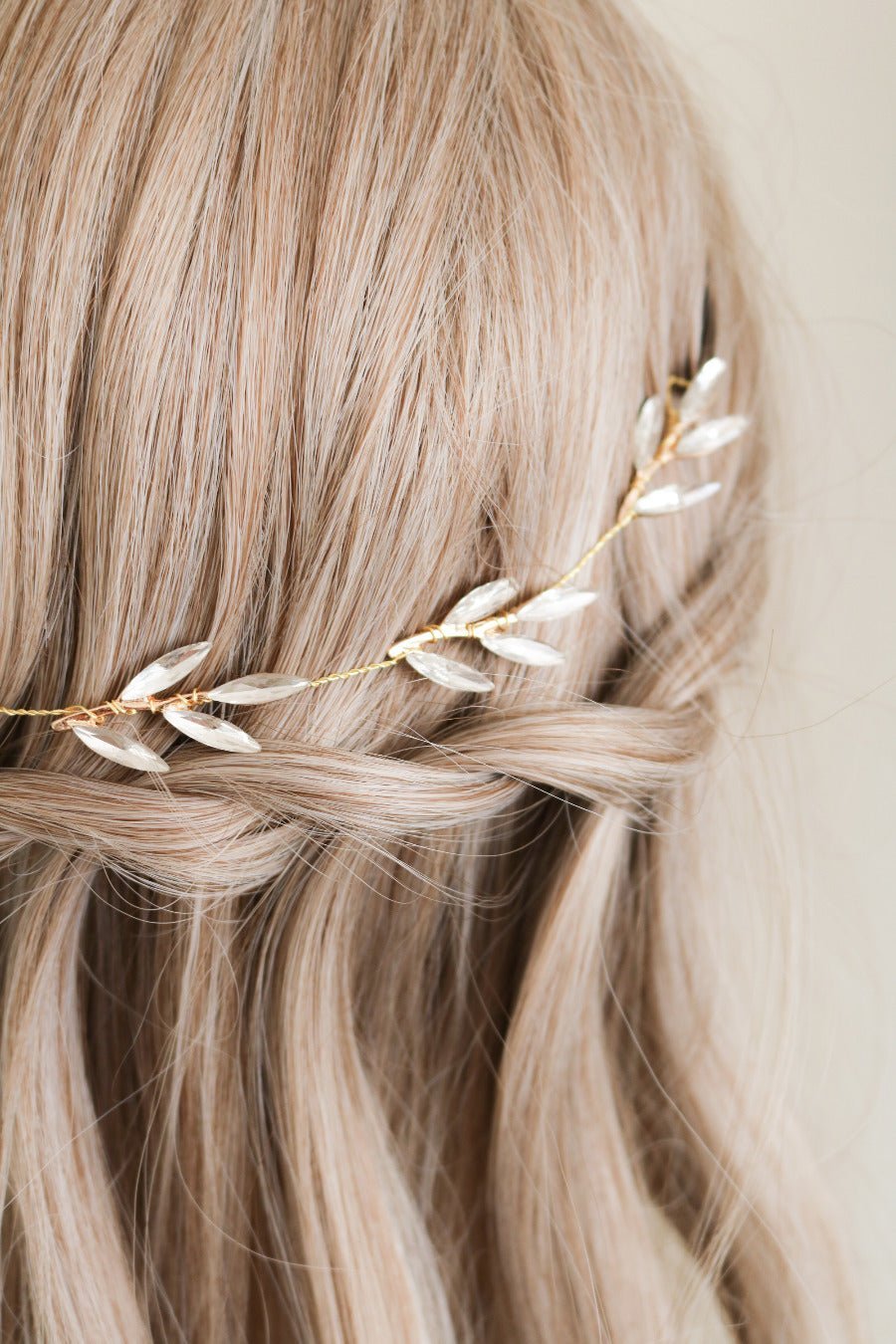 A close up view of a gold wire wrapped hair piece with crystal leaves sitting in a braided bride's hair. 