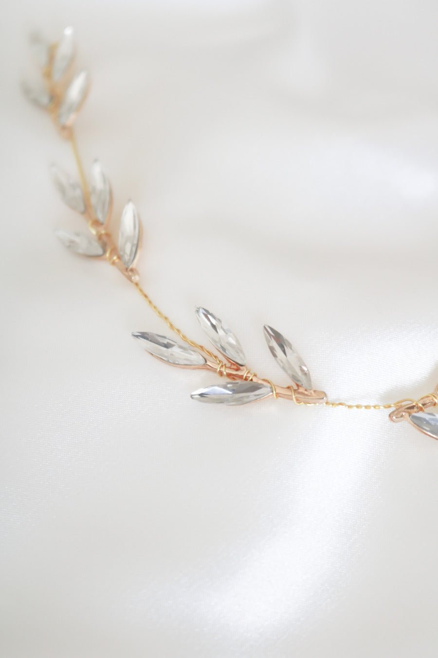 Detailed close up of a golden wire-wrapped hairvine with crystal leaves against white satin background. 