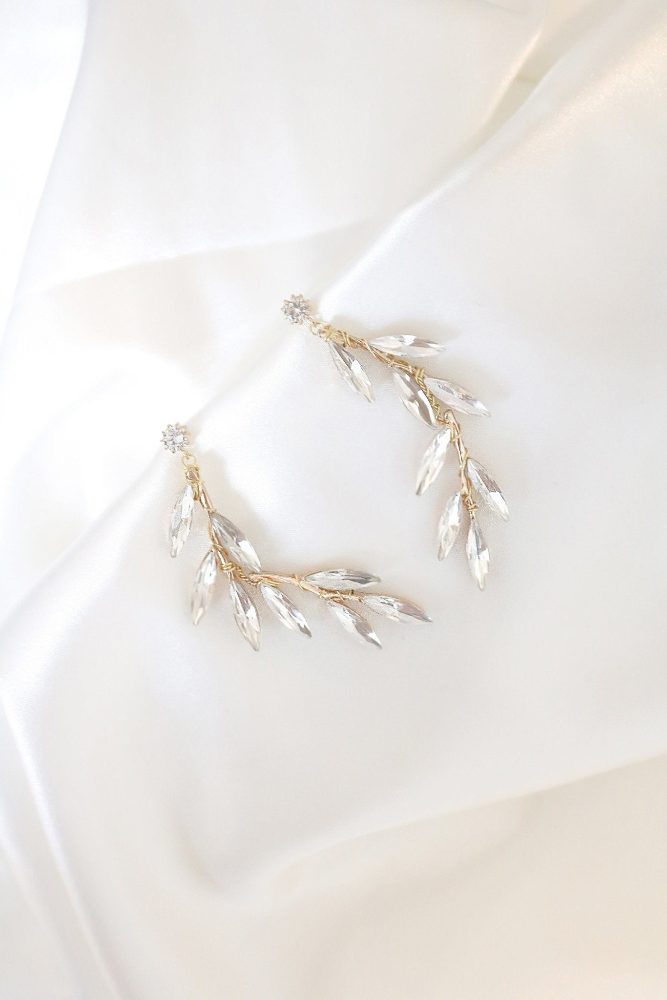 Crystal leaf golden studded earrings on satin display. 