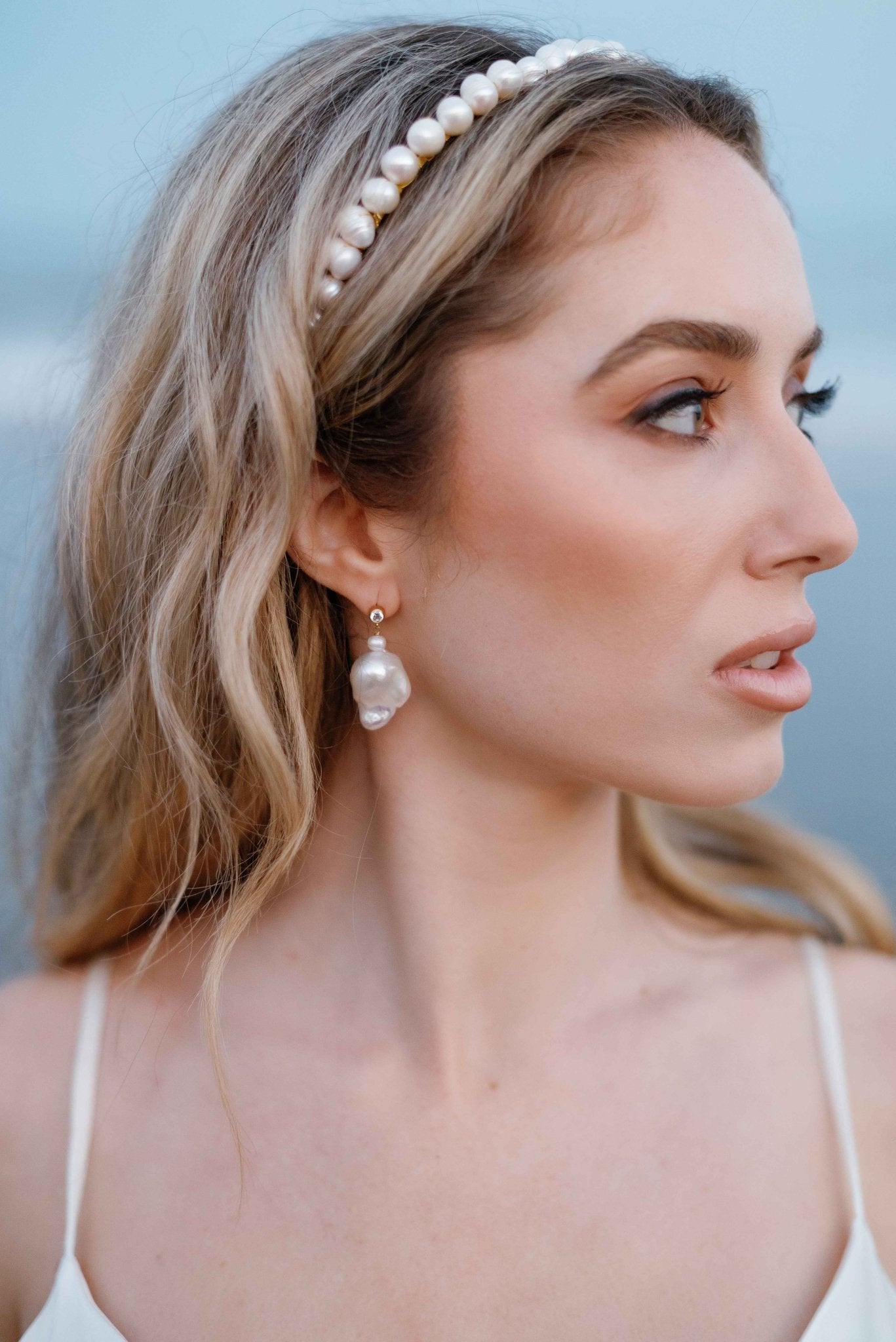 A bride looks off to the side while wearing a bridal headband and Baroque freshwater pearl stud earrings with cubic zirconia. 