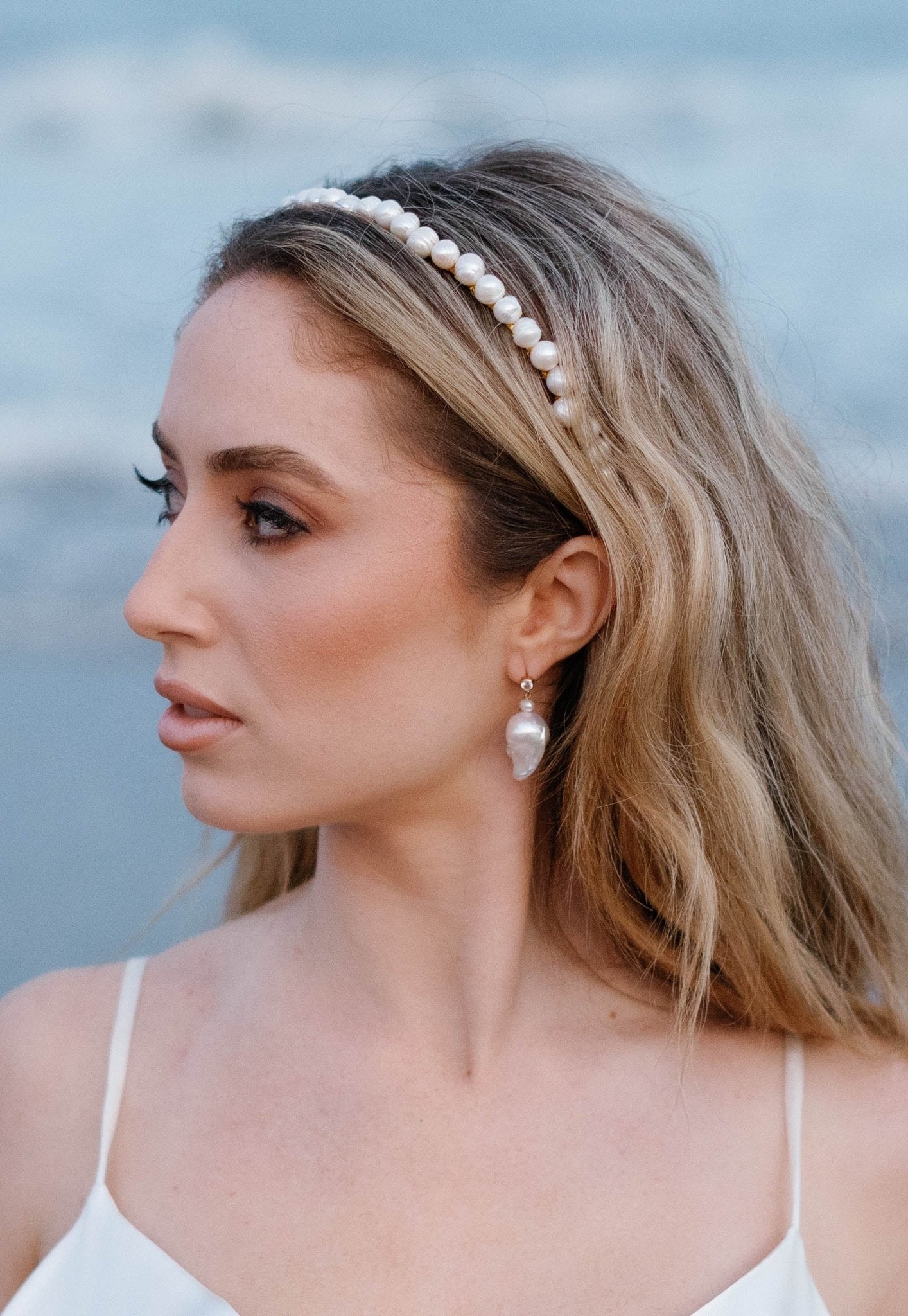 A bride looks off to the side while wearing a bridal headband and Baroque freshwater pearl stud earrings with cubic zirconia. 