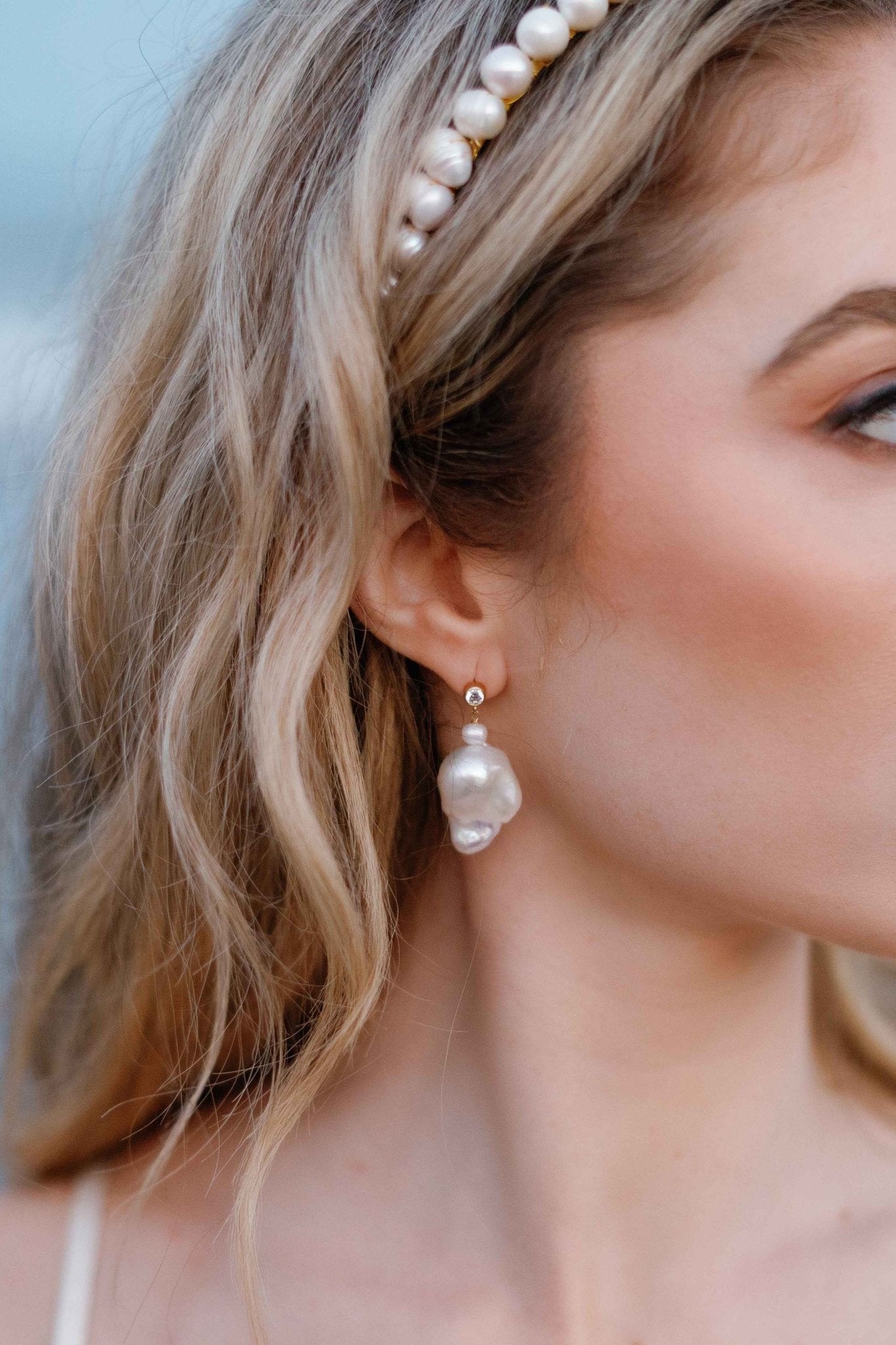 A close up of a bride looking off to the side while wearing a bridal headband and Baroque freshwater pearl stud earrings with cubic zirconia. 