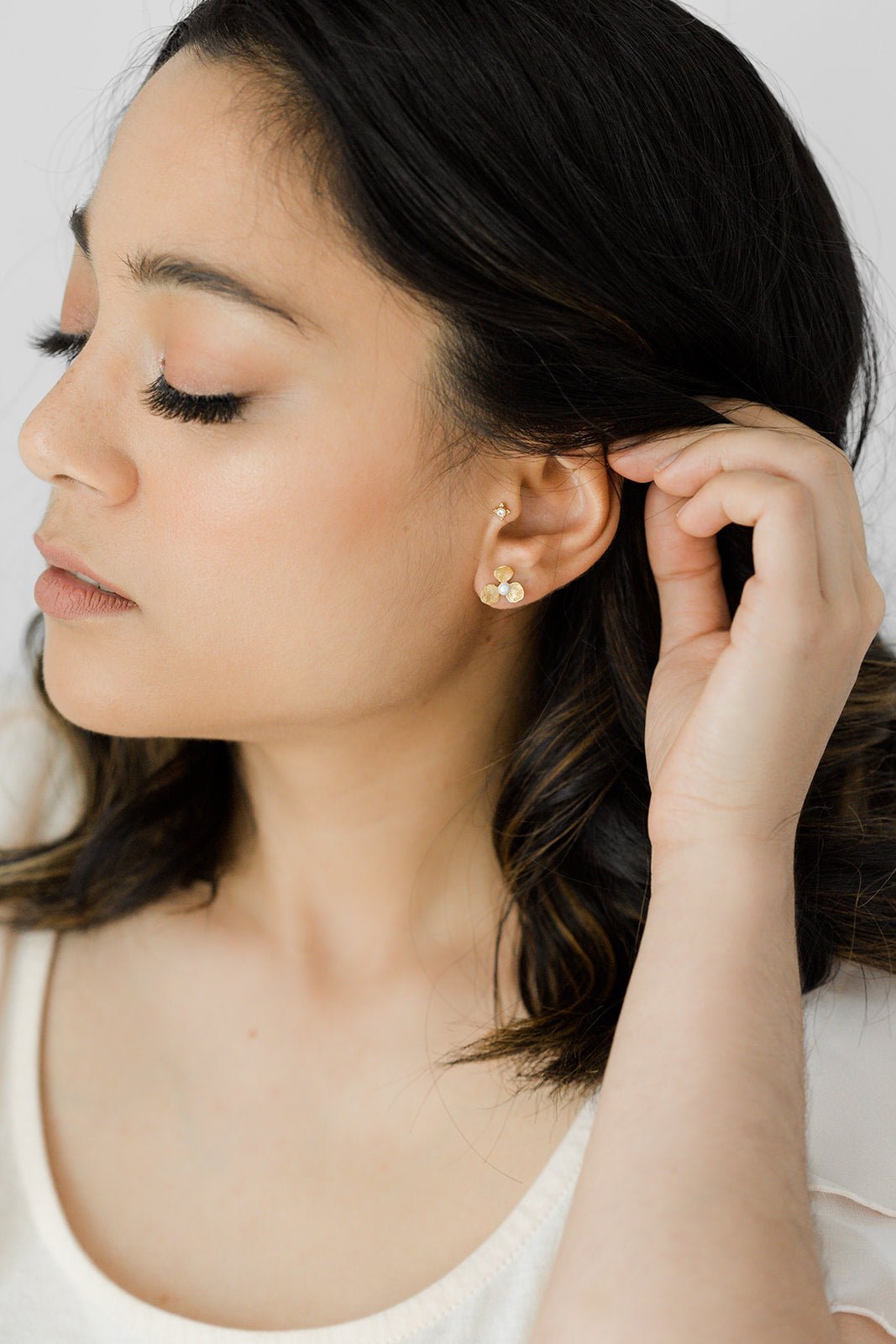 Bella Flower studs with freshwater pearls in gold-filled with sterling silver posts being worn by a woman holding some of her hair back.