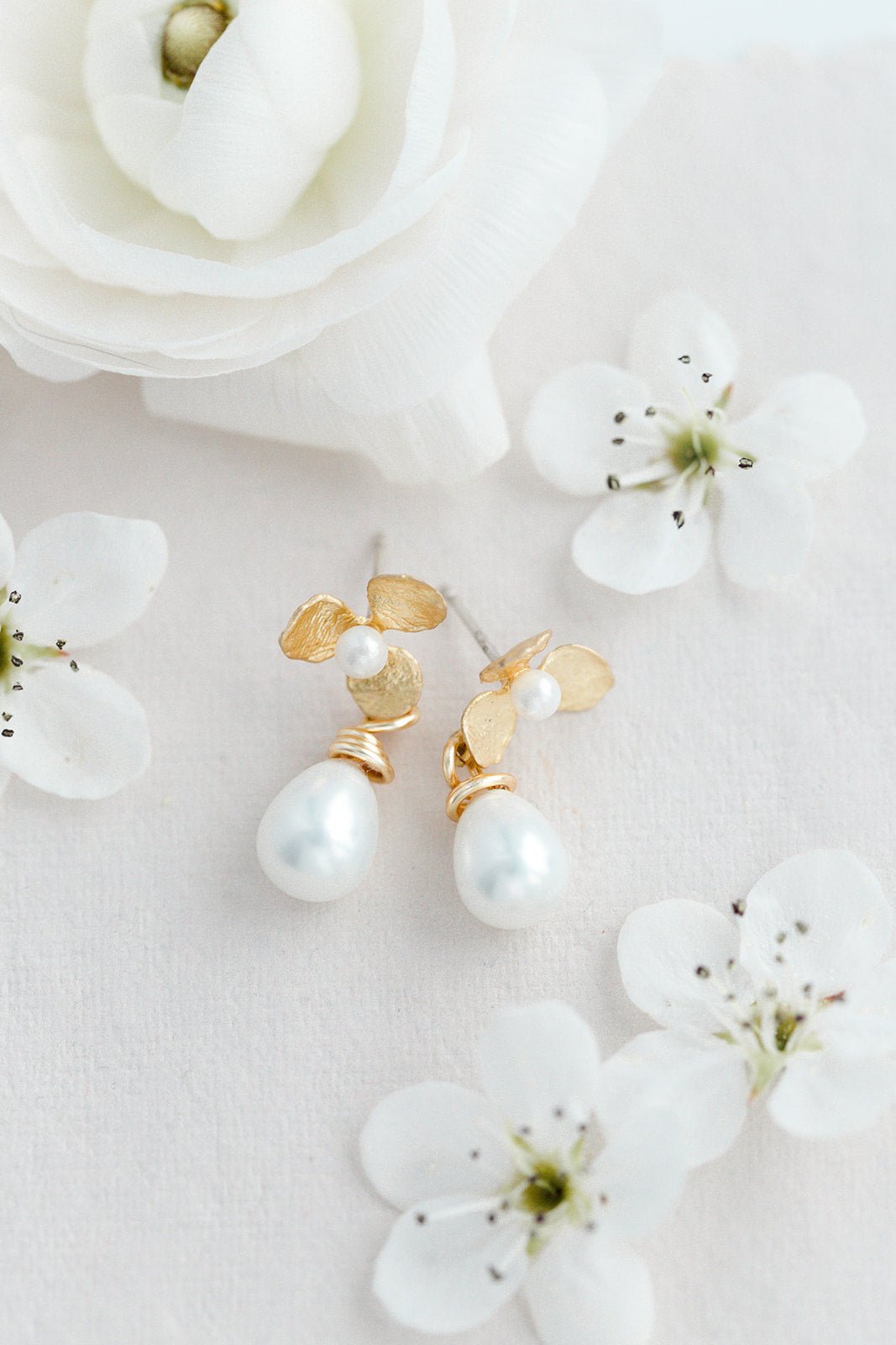 Bella Flower & Drop Pearl Earrings surrounded by white flowers. Bridal jewelry Canada. Pearl jewelry Canada. Pearl Bridal jewelry Canada. Gold-filled jewelry Canada. Gold-filled Canadian jewelry. Handmade Canadian jewelry. Canadian handmade jewelry. Small Canadian jewelry brands. Canadian jewelry brands.