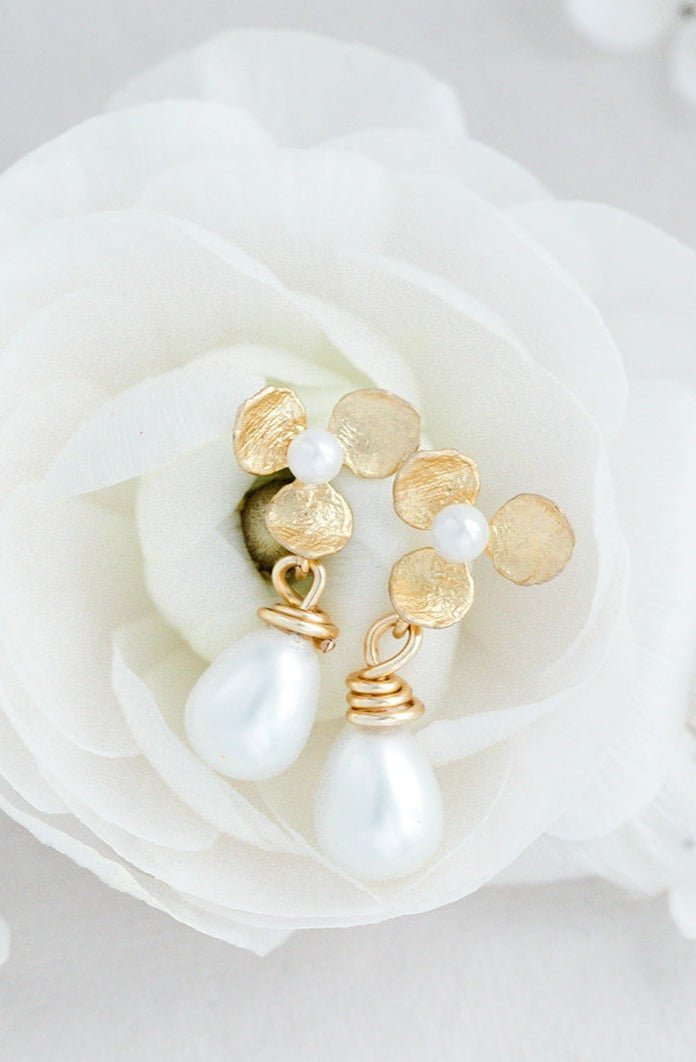 A Close Up of Bella Flower & Drop Freshwater Pearl Earrings with Sterling Silver Posts and Gold-Filled Flowers sit inside a white rose. 