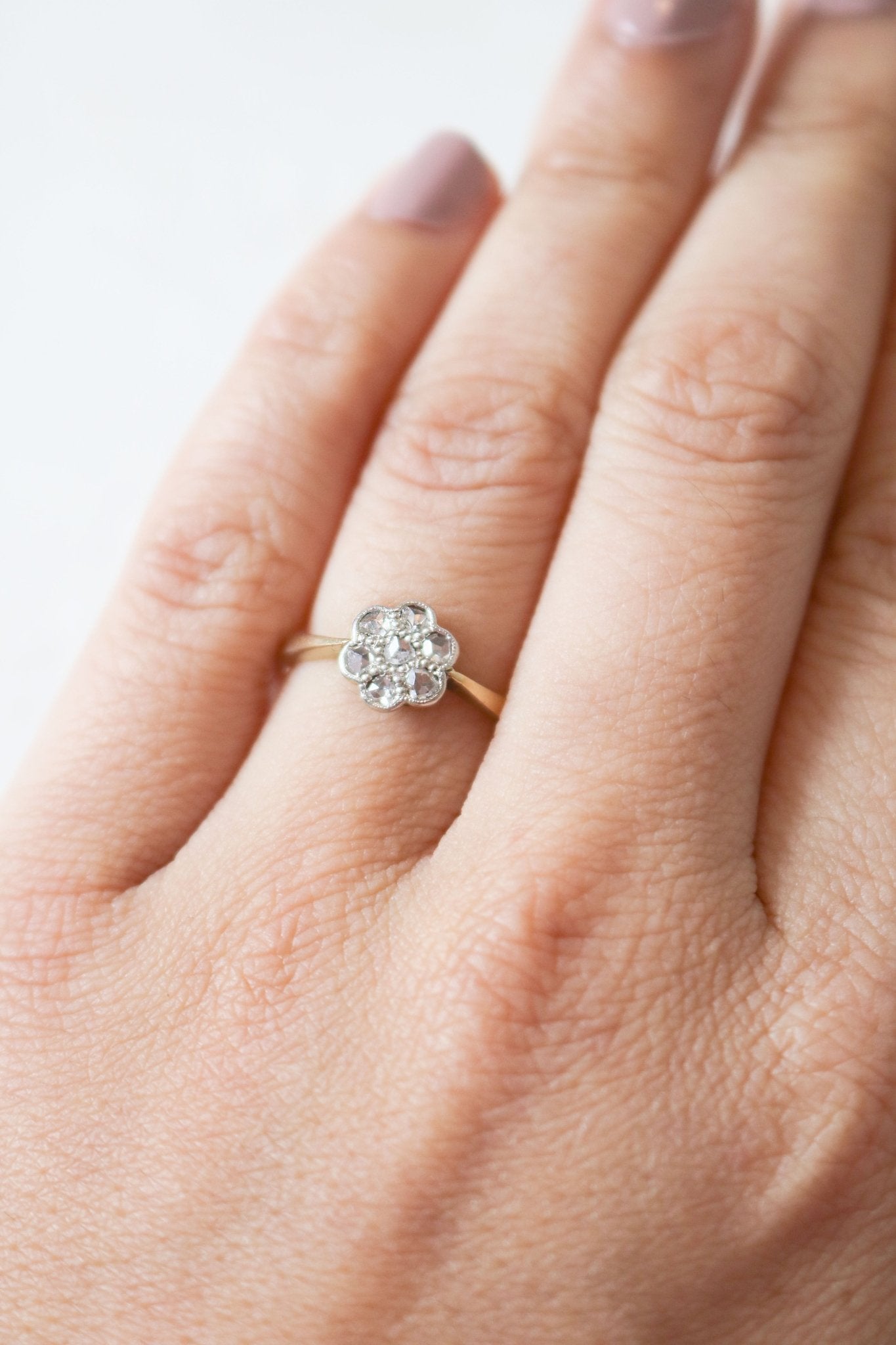 An 18ct gold vintage engagement ring with a flower inset with diamonds on a ring finger. 