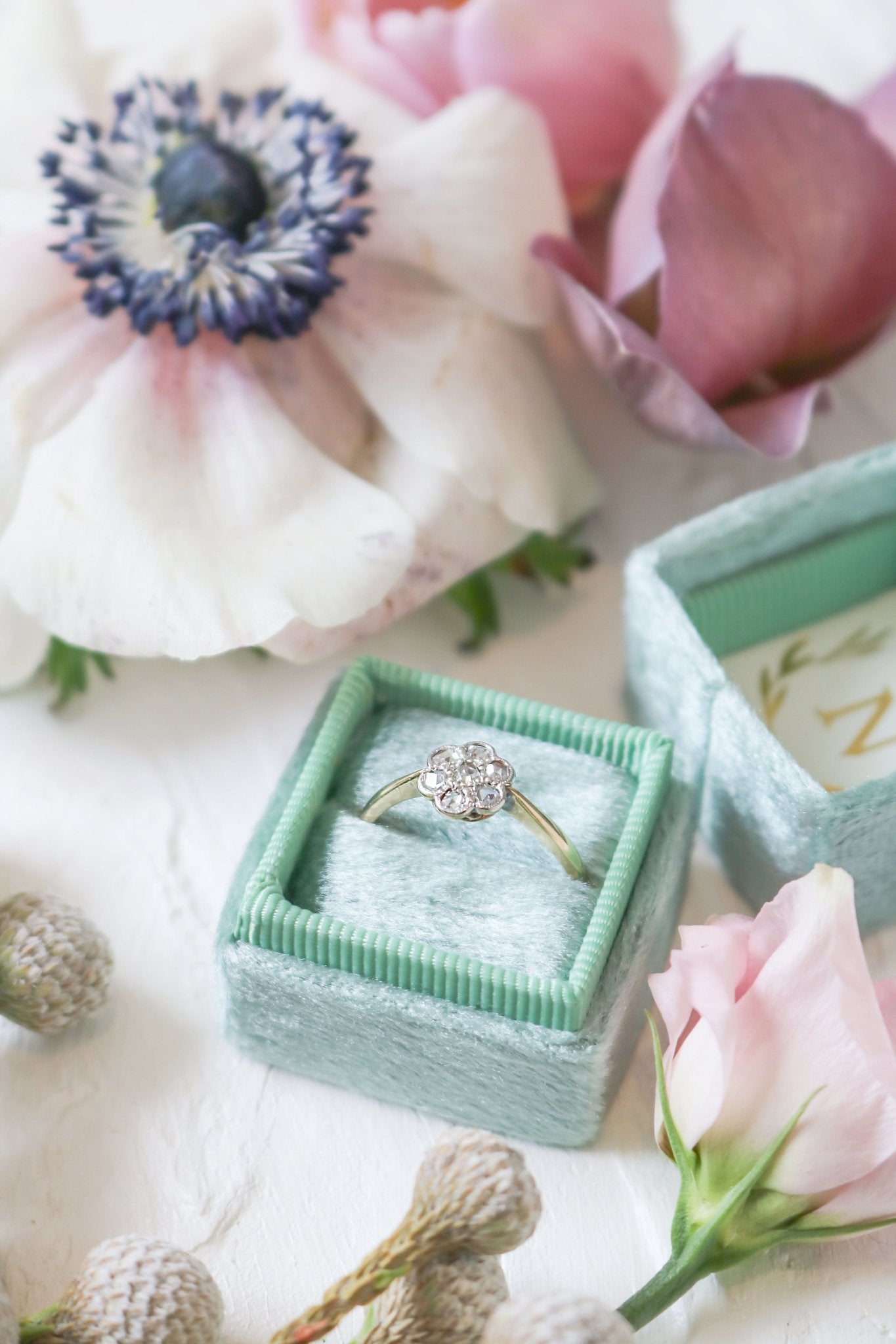 Betony Diamond Flower Vintage Engagement Ring in 18ct Yellow Gold and Platinum sitting in a ring box surrounded by flowers. 