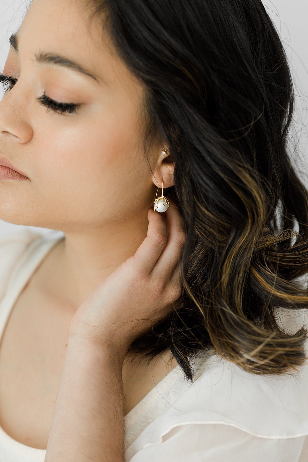 A Bloom Flower Bud Freshwater Pearl Earring hangs from a woman's ear. 