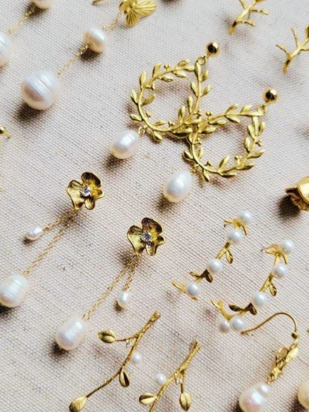 A selection of gold-filled freshwater pearl floral bridal earrings on a linen background