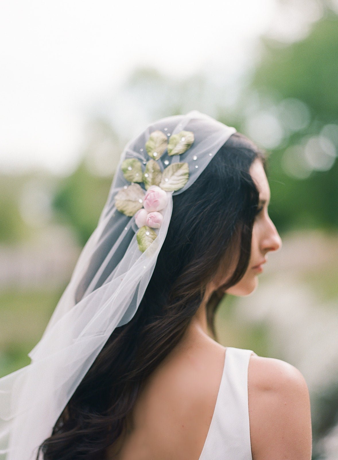 A long veil is somewhat bunched at the sides with flowers, leaves, and dotted with crystals to look like dew.