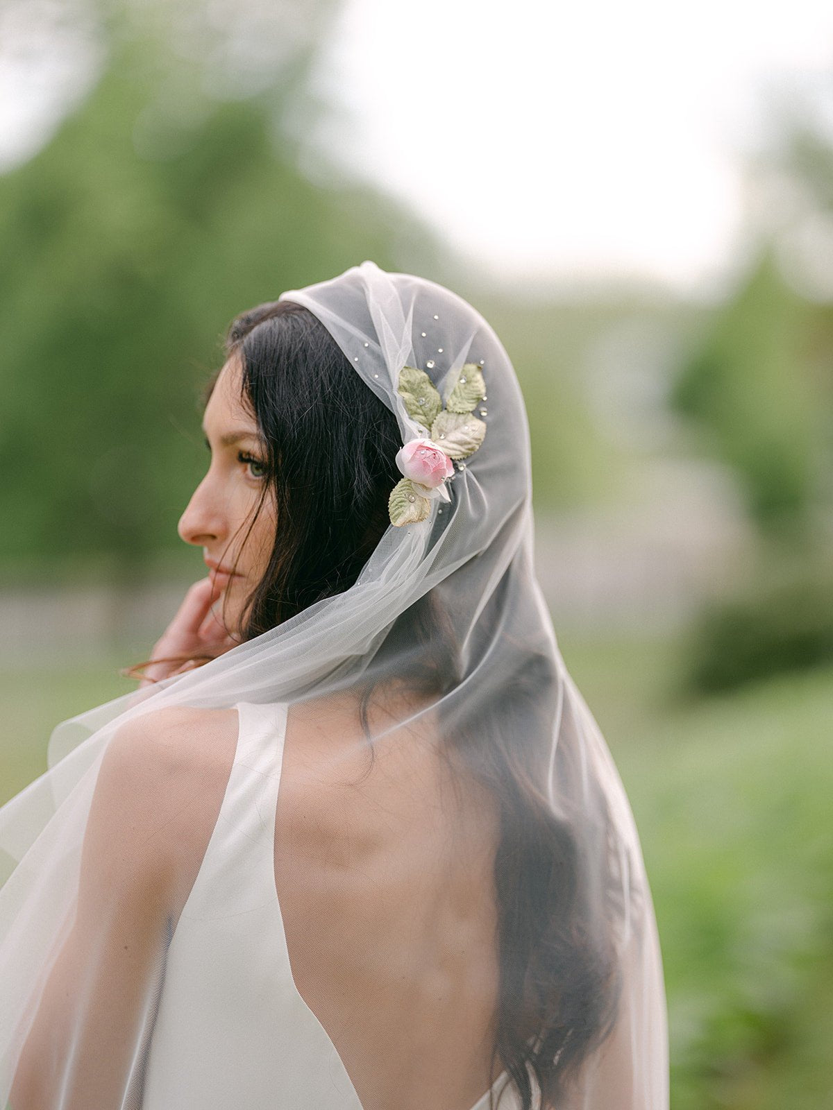 A bride looks curiously out of frame, her back brushed by the soft Italian tulle decorated wedding veil. 