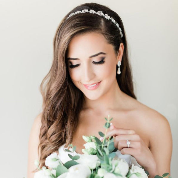 A beautiful brunette bride looking down at her bridal bouquet while wearing a silver crystal bridal headband and sterling silver bridal earring with freshwater pearl. Bridal hair accessories & silver wedding jewelry Canada