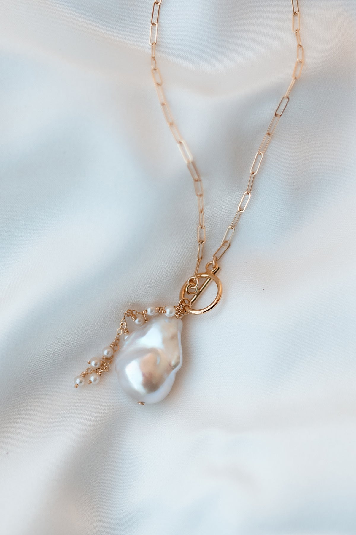 Gold-filled necklace with large baroque pearl pendant on fabric background. Pearl Bridal jewelry Canada. Organic pearl jewelry.