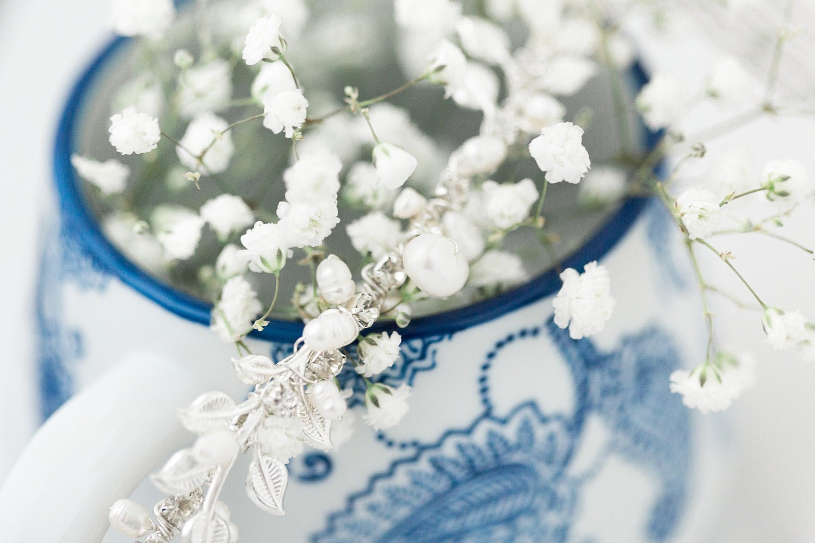 Silver Byrony Fresh Water Pearl and Crystal Leaf Hairvine tucked around a flower vase with Baby's Breath. 