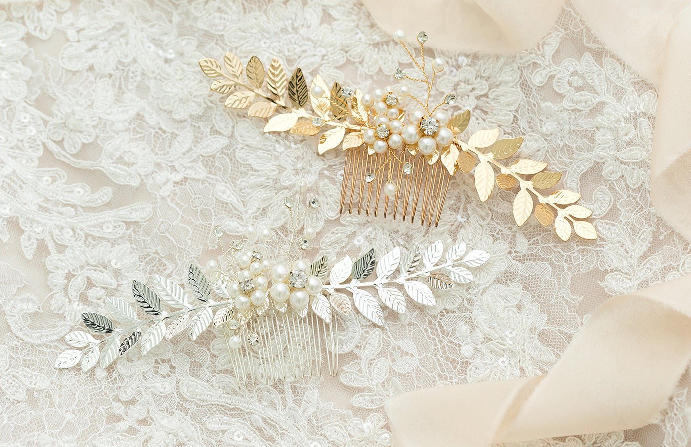 Two bridal hair combs with freshwater pearls, crystals, and golden leaves lays on a length of lace above a silver one.  