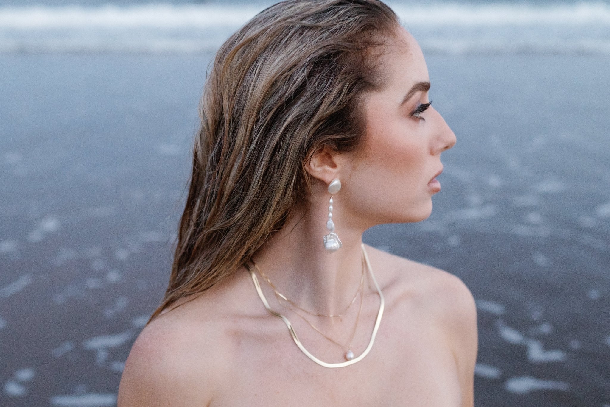 A beautiful modern goddess wearing gold-filled necklaces; a herringbone chain, a stacking chain, and a pearl necklace. She has different freshwater pearls in a dangle earring.