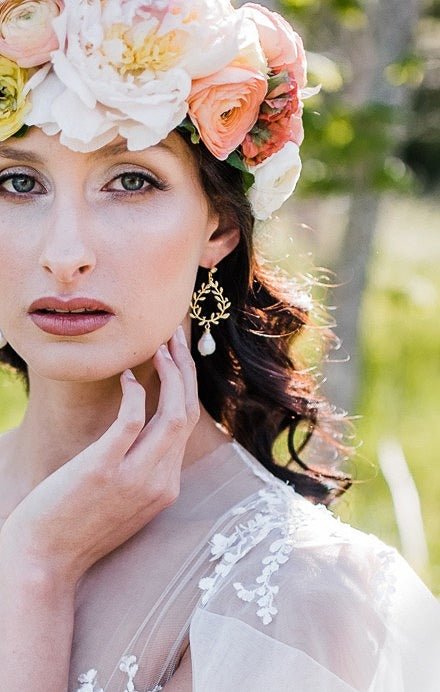 A blooming bride with a flower wreath lightly touches her face to bring attention to the gold-filled laurel leaf bridal earrings with freshwater pearl drops and crystal studs. Bridal jewelry Canada. Pearl jewelry Canada. Pearl Bridal jewelry Canada. Gold-filled jewelry Canada. Organic pearl jewelry. Canadian jewelry brands.  